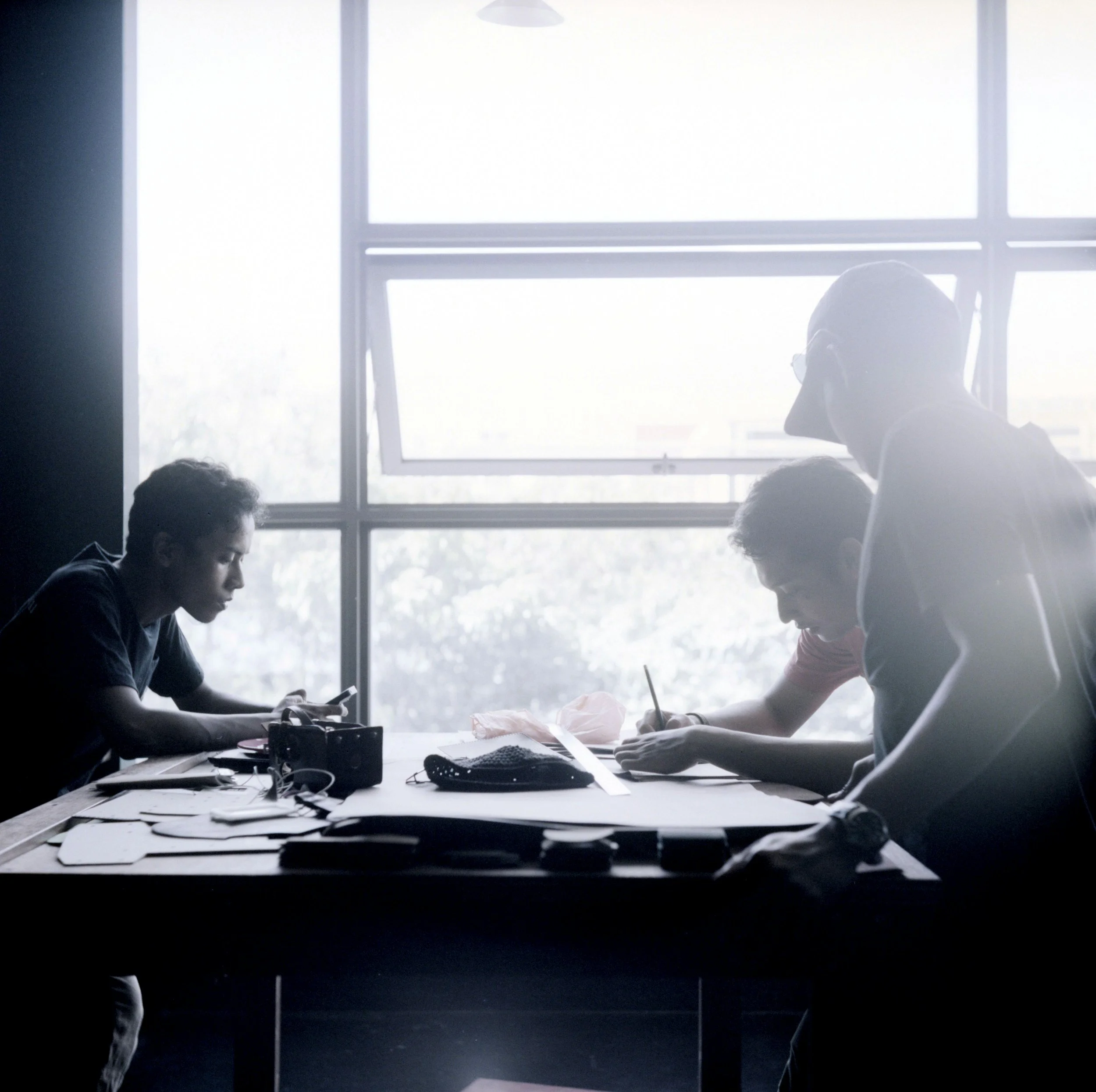 People sitting at a table working on a project in a room with large windows letting in natural light.