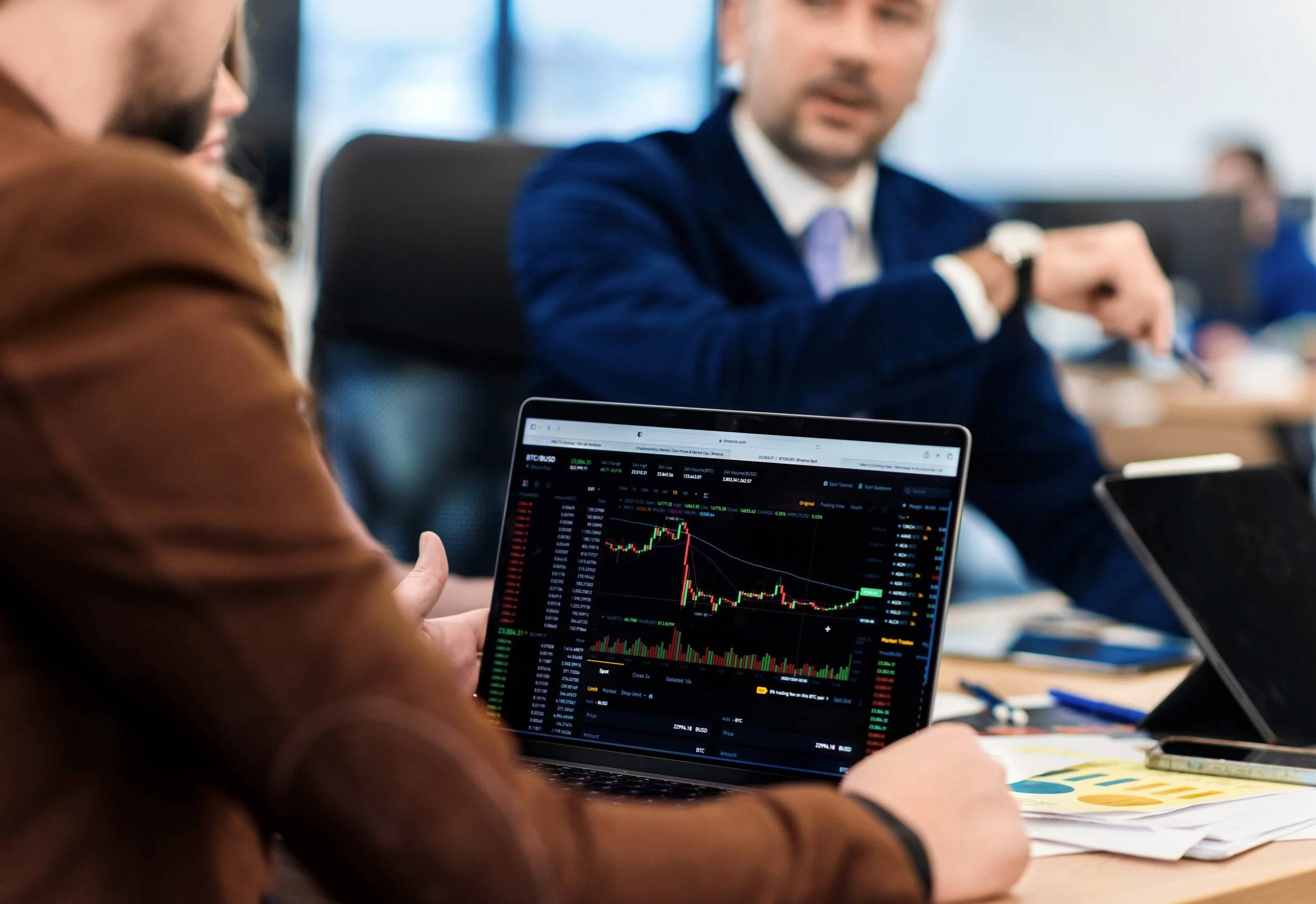 A person holding a tablet displaying a Bitcoin to USD trading chart during a business meeting.
