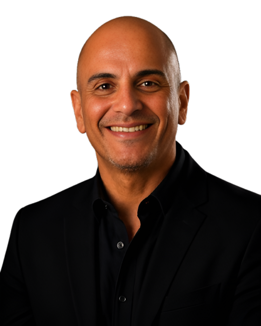 Smiling man with a shaved head wearing a black suit and black shirt against a black background.