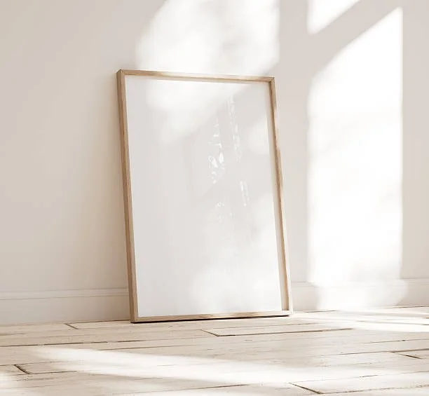 Empty frame leaning against a wall with sunlight and shadows in a minimal room.