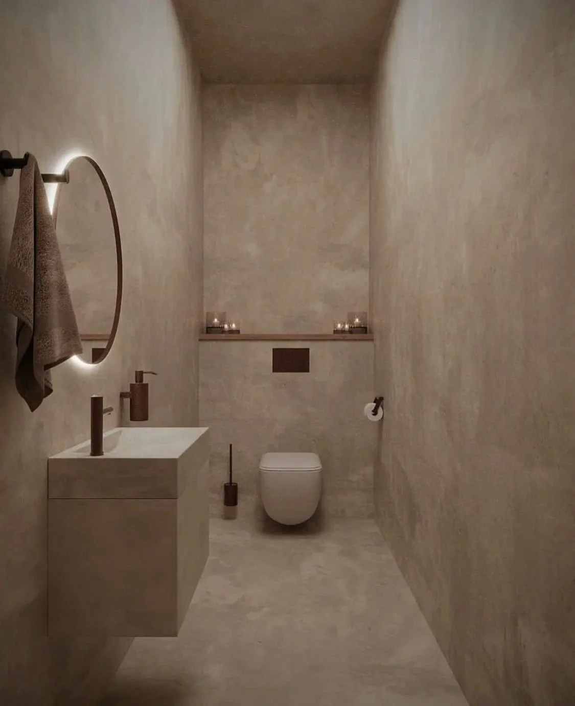 Minimalist bathroom with beige textured walls and floor, a wall-mounted toilet, a small built-in shelf with candles, a round mirror with a backlit glow, a towel hanging on a hook, and a vanity with a modern sink.