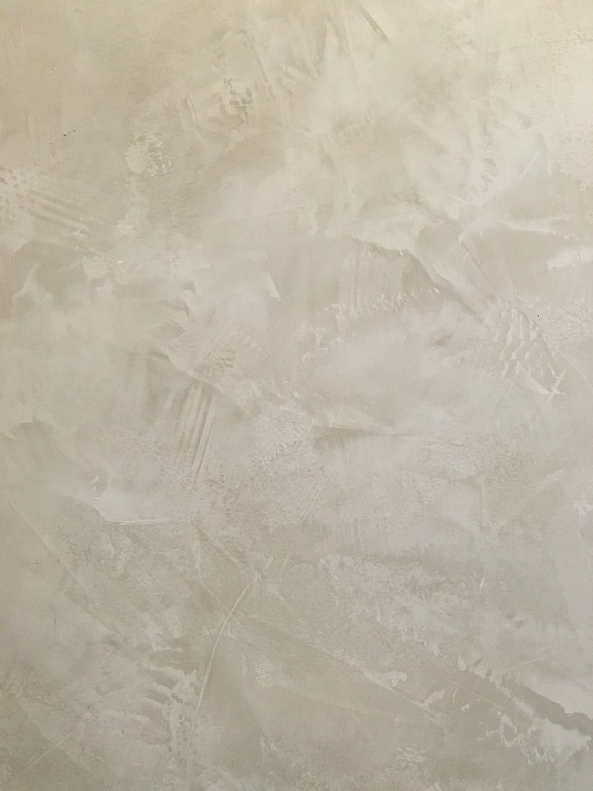 A close-up of a textured wall with a beige or light cream color and visible brushstrokes or plastering patterns.