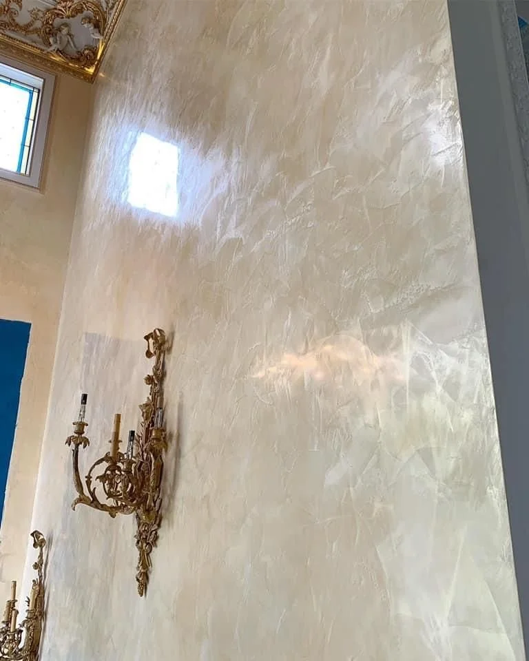 Interior wall with a gold chandelier and a window with stained glass at the top.