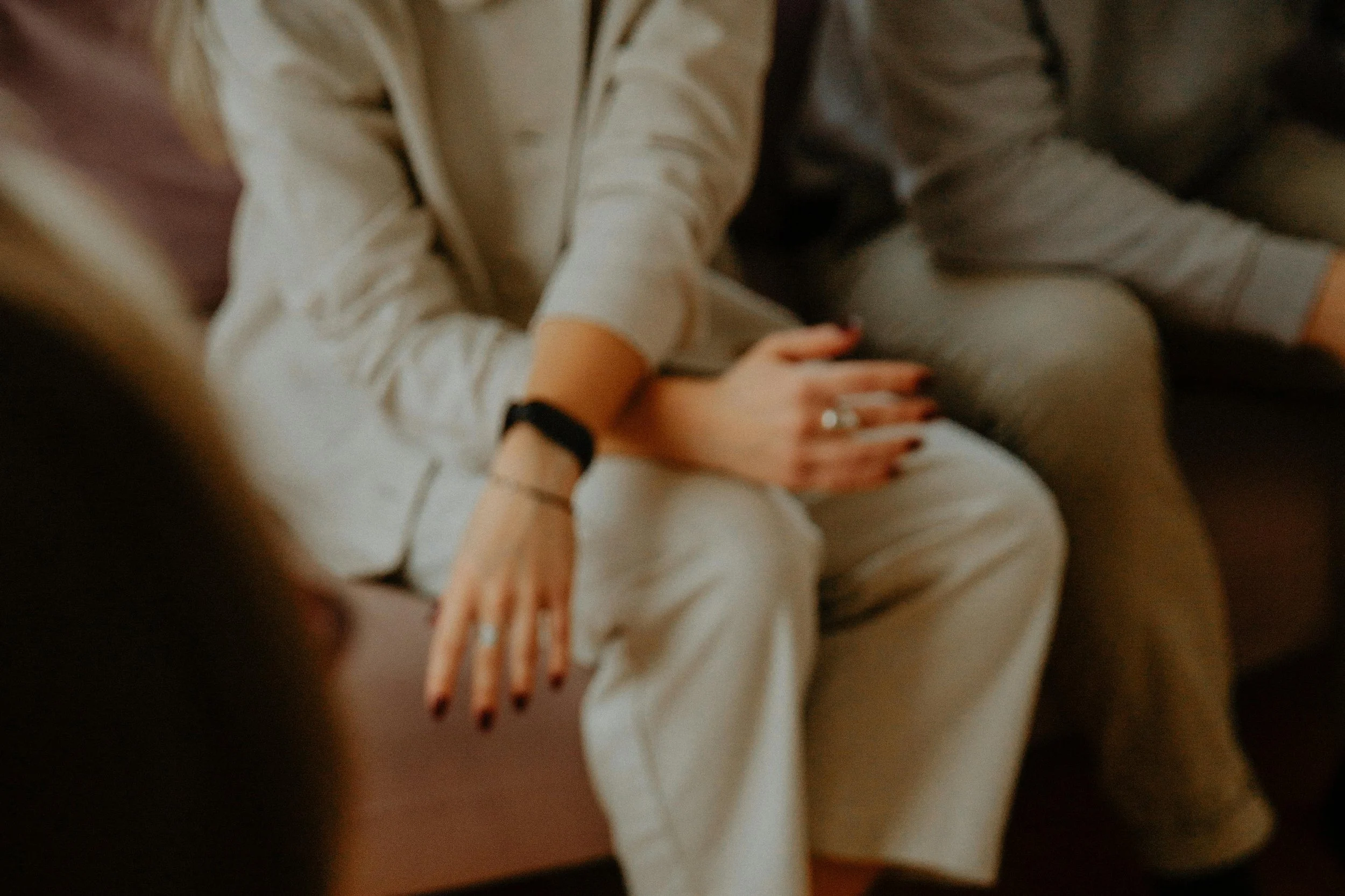 A person wearing a beige hoodie, sitting with their legs crossed, with multiple hands resting on their legs.