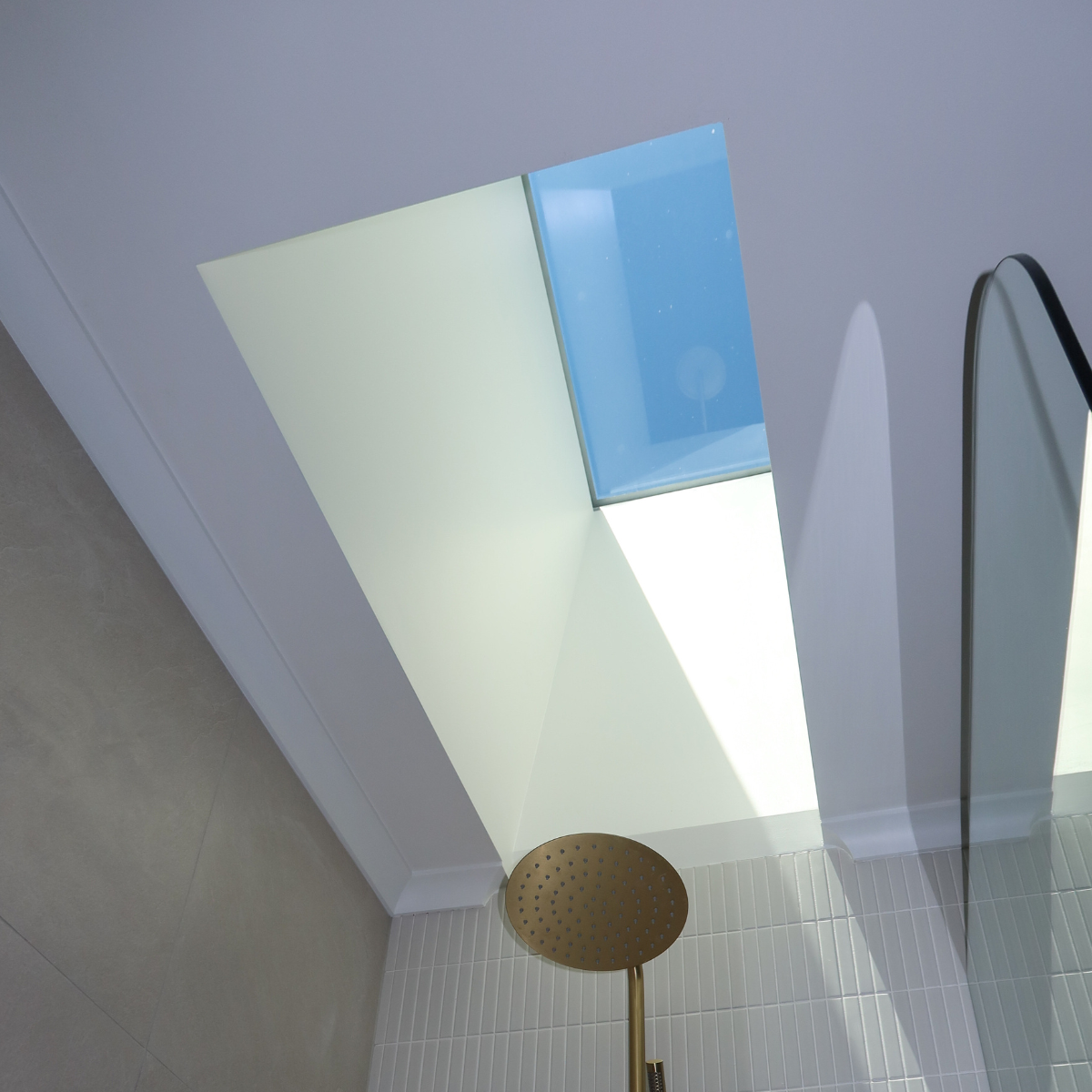 Modern shower area with a rain shower head, white tiled floor, a wall with a window, and partial views of mirrors.