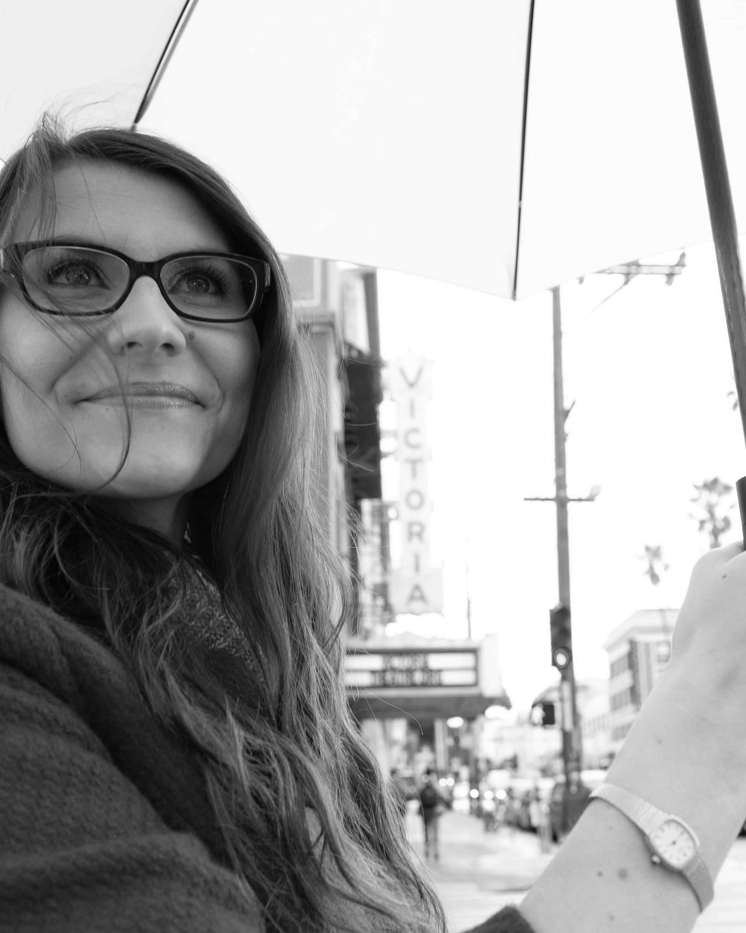 Victoria Hanson in San Francisco in front of the Victoria Theatre holding an umbrella.