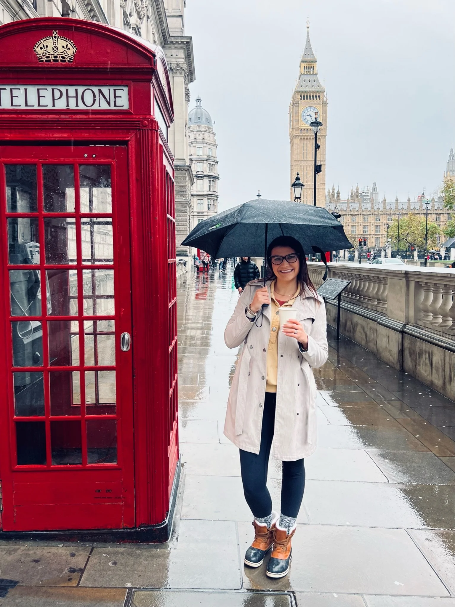 Victoria Hanson in London near Big Ben, in front of a red telephone box, holding an umbrella.