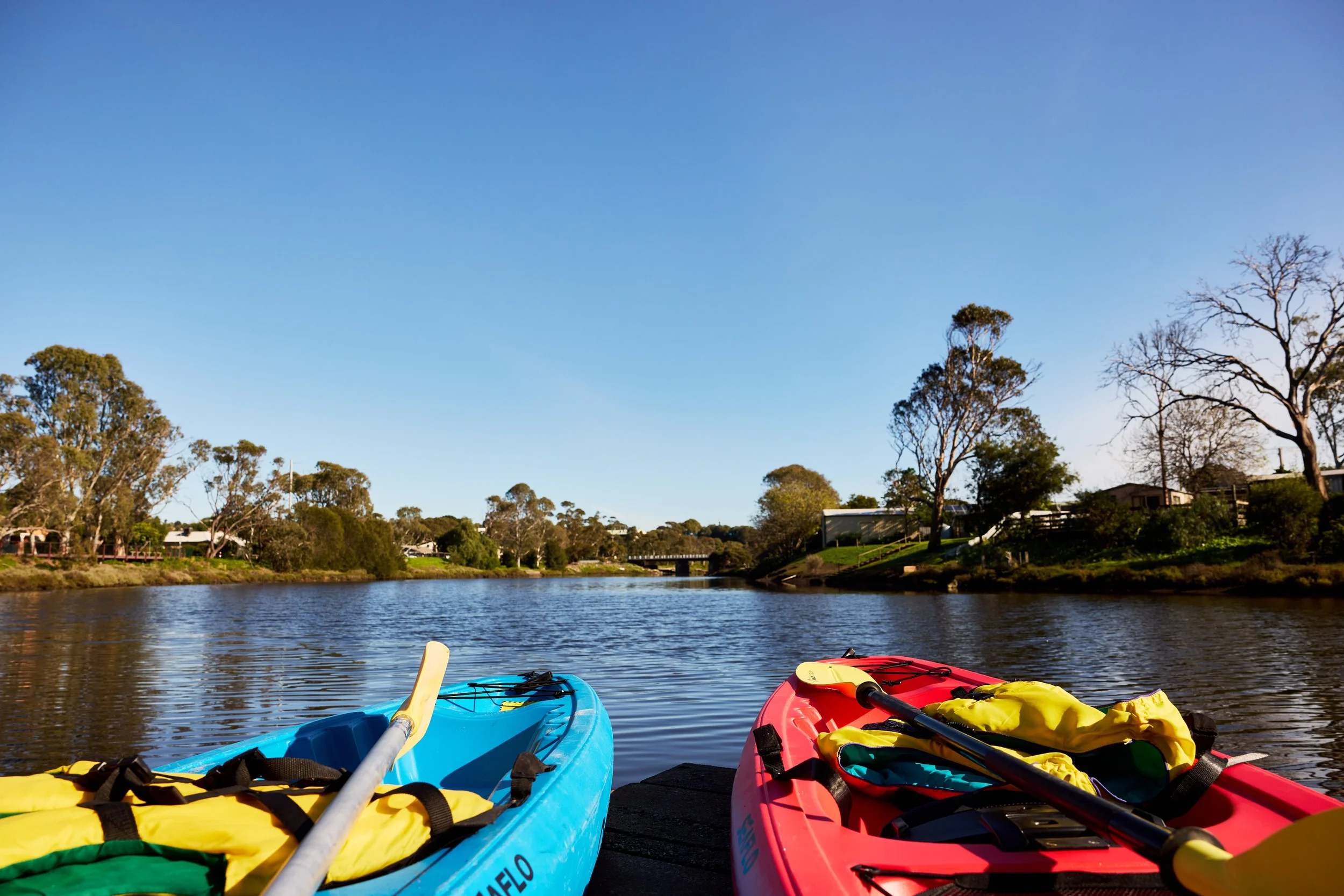 Kayaks on a calm river with trees and a clear blue sky in the background.