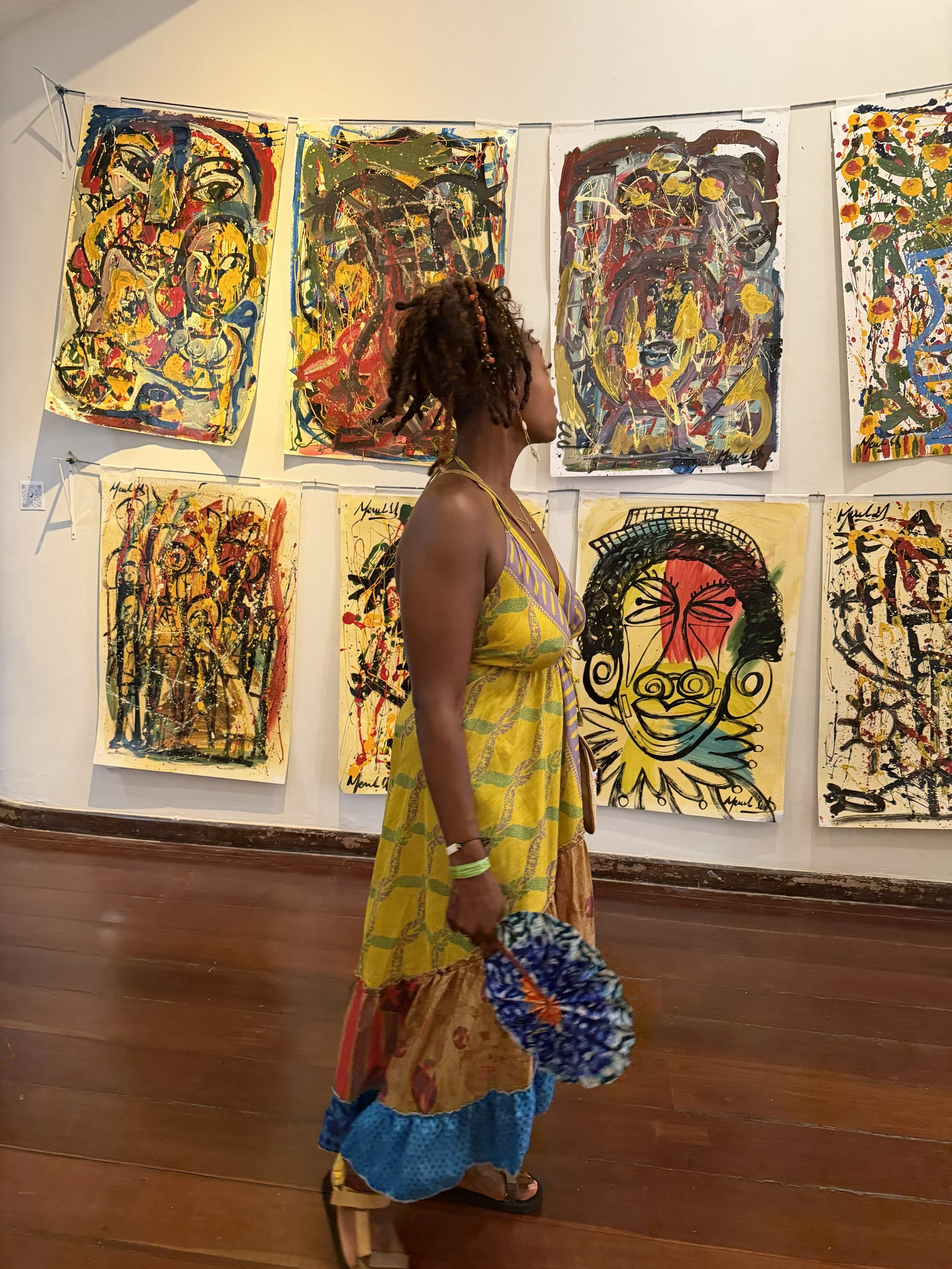 A woman with braided hair standing in front of abstract paintings in an art gallery.
