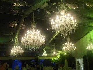 L'image montre un plafond orné de plusieurs grands chandeliers en cristal éclairés, avec un éclairage vert tamisé, dans une salle décorée élégamment.
