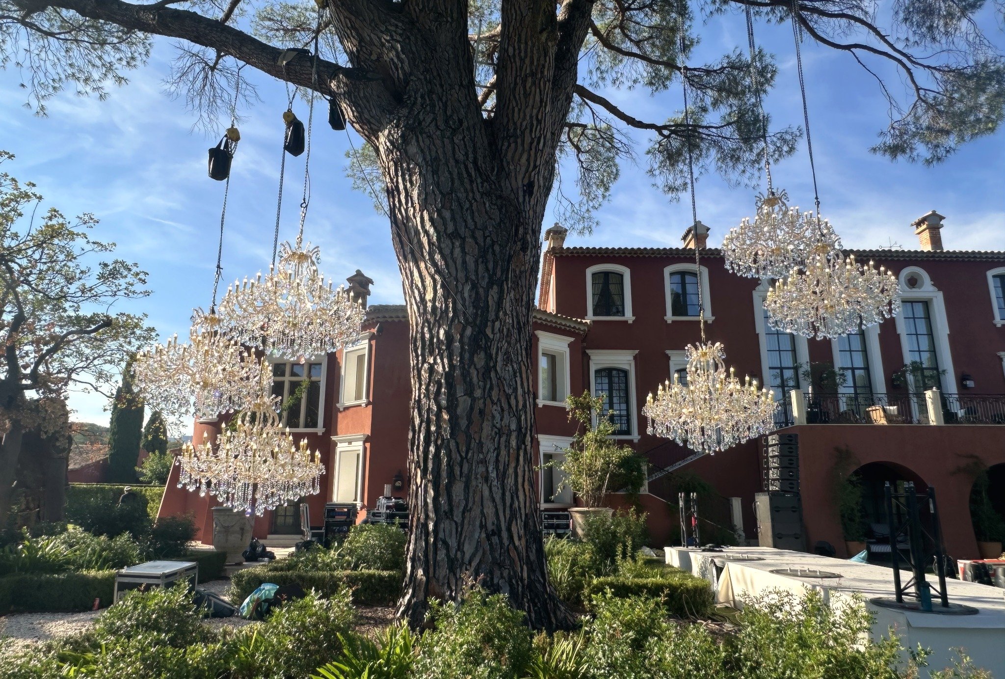 Un grand arbre avec des lustres suspendus de ses branches, en arrière-plan une maison de style européen avec plusieurs fenêtres.