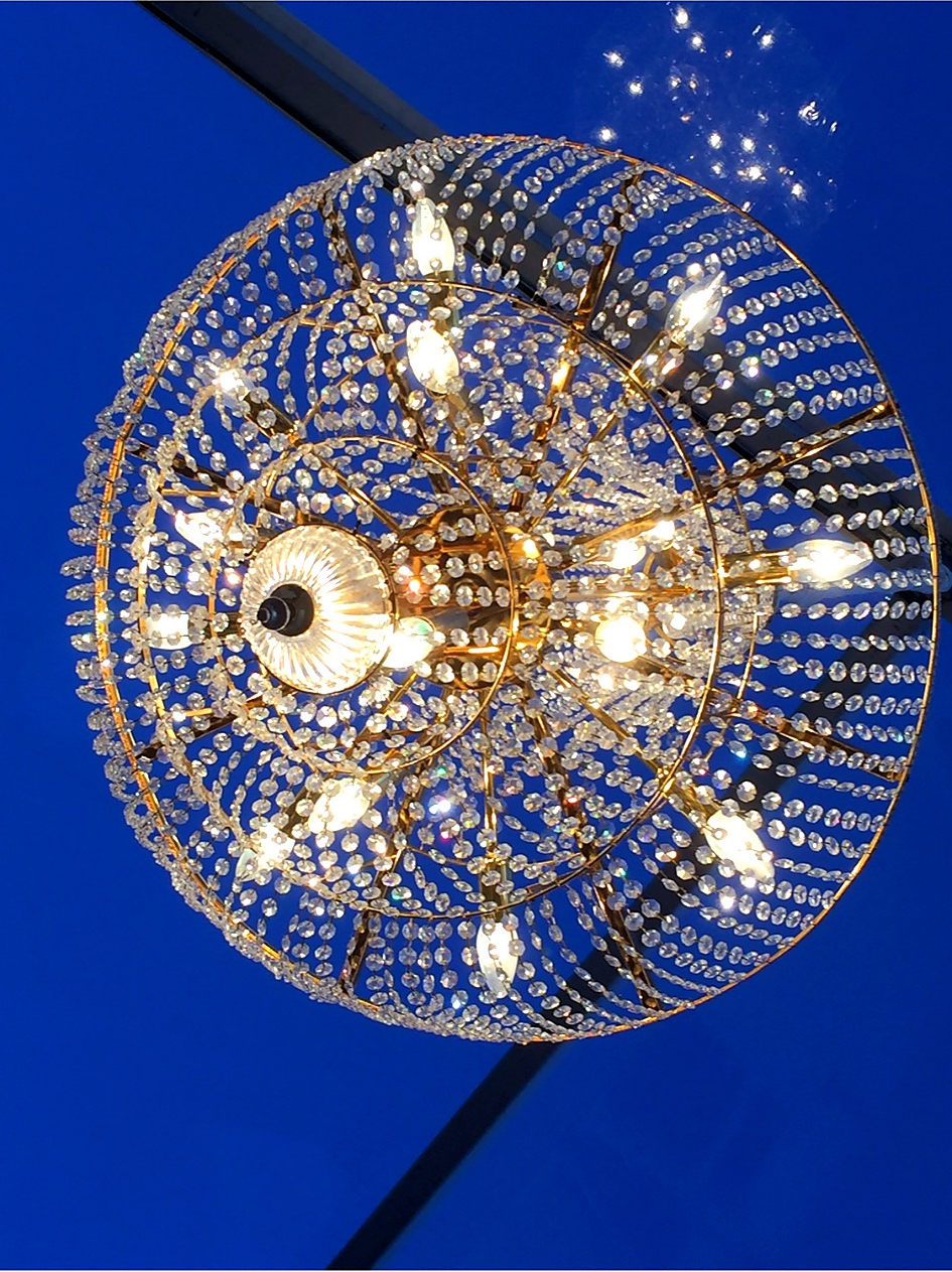 Un chandelier élégant avec des cristaux suspendus et des ampoules allumées, vu contre un plafond bleu.