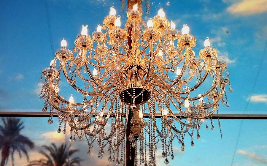 Un grand lustre en cristal suspendu sous un plafond en verre, avec un ciel bleu en arrière-plan.