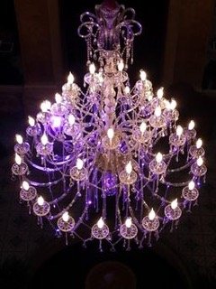 Grand chandelier en cristal avec lumières violettes et blanches.