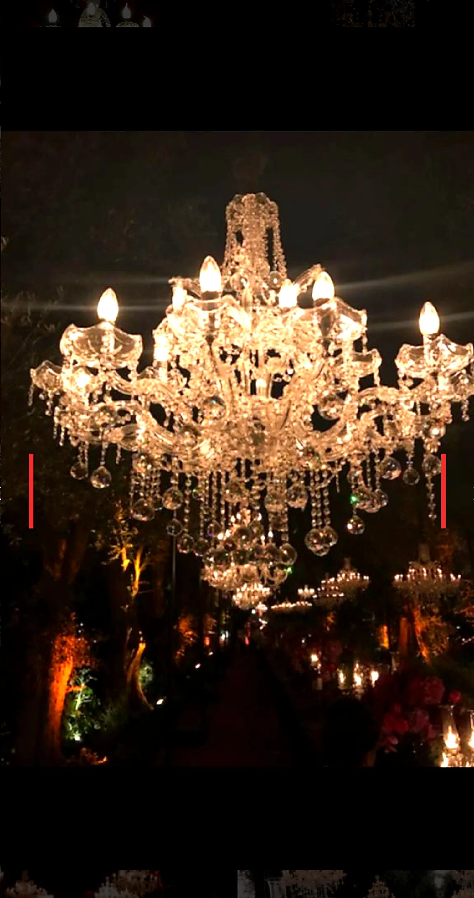Un lustre en cristal brillant suspendu dans un endroit sombre, décoré avec des lumières chaudes et d'autres lustres en arrière-plan.