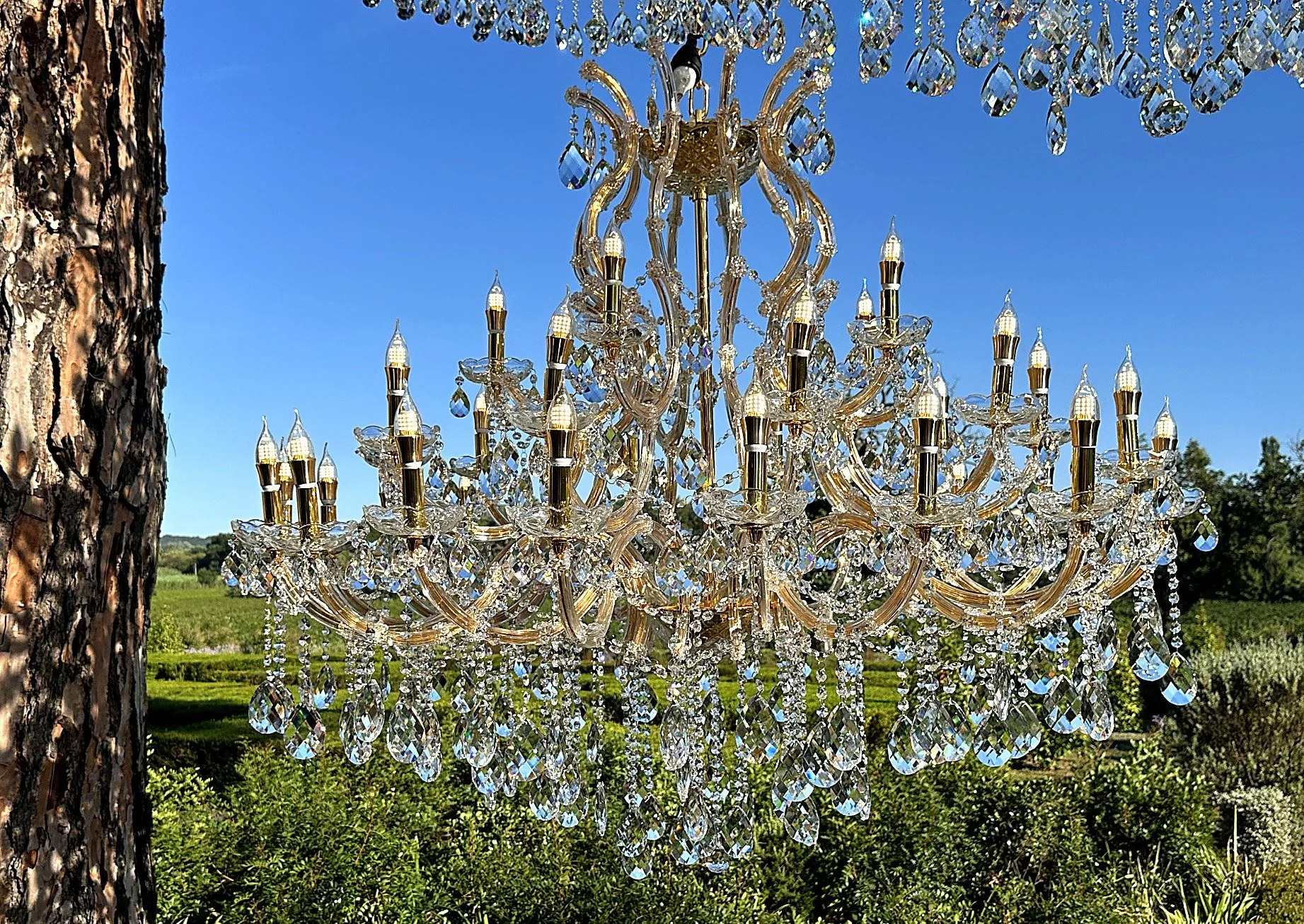 Un chandelier en crystal suspendu à l'extérieur avec un arbre et un ciel bleu en arrière-plan.