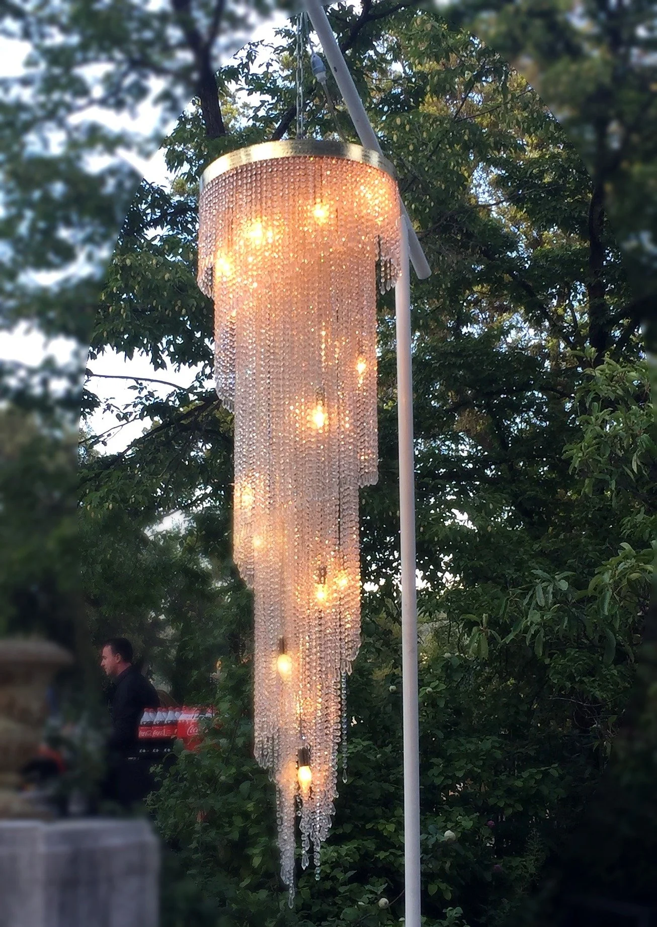 Un lampadaire décoratif orné de cristaux suspendus, illuminé dans un environnement extérieur avec des arbres en arrière-plan.