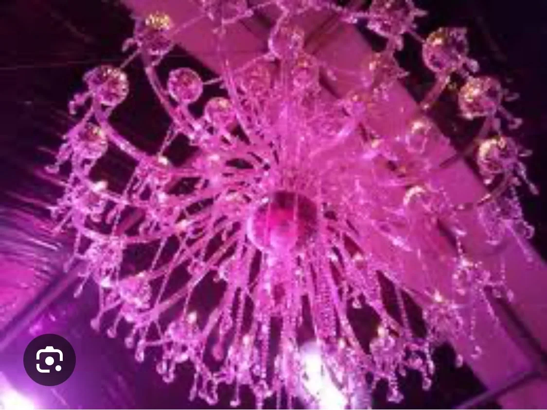 Un lustre chandelier rose brillant suspendu au plafond dans une pièce sombre.