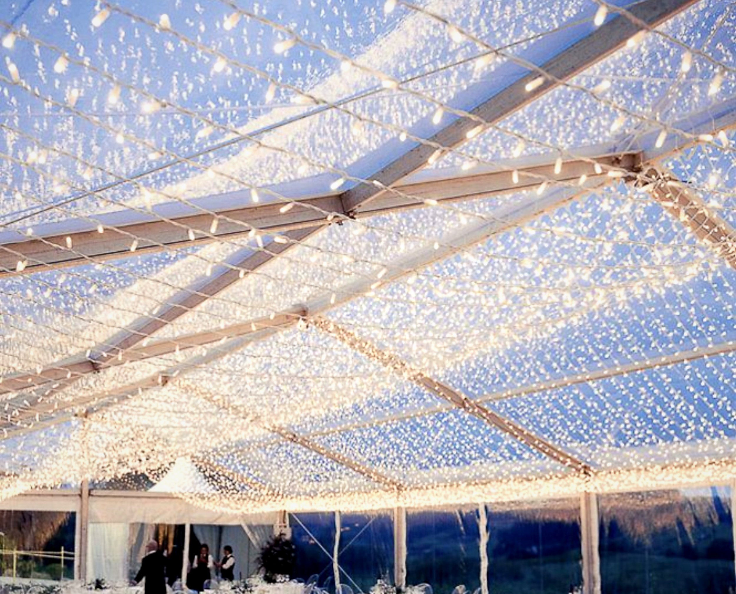 Structure de décoration d'éclairage suspendue faite de câbles de fer recouverts de guirlandes lumineuses en forme de petites ampoules, dans un espace intérieur ou extérieur, créant une ambiance chaleureuse.
