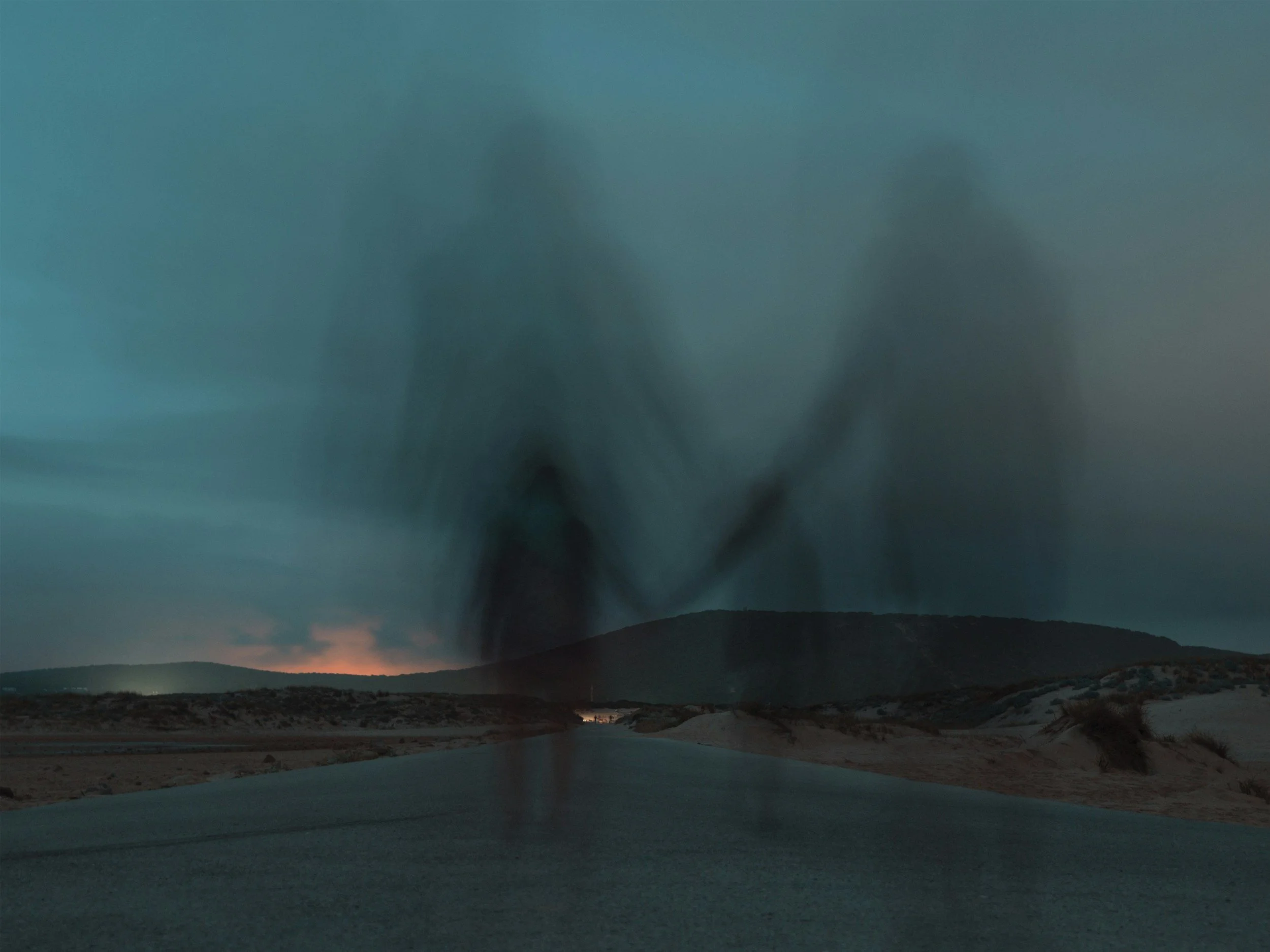 A landscape view of a desert with mountains under a sky with green and purple hues, and a large tornado or dust devil visible in the distance.