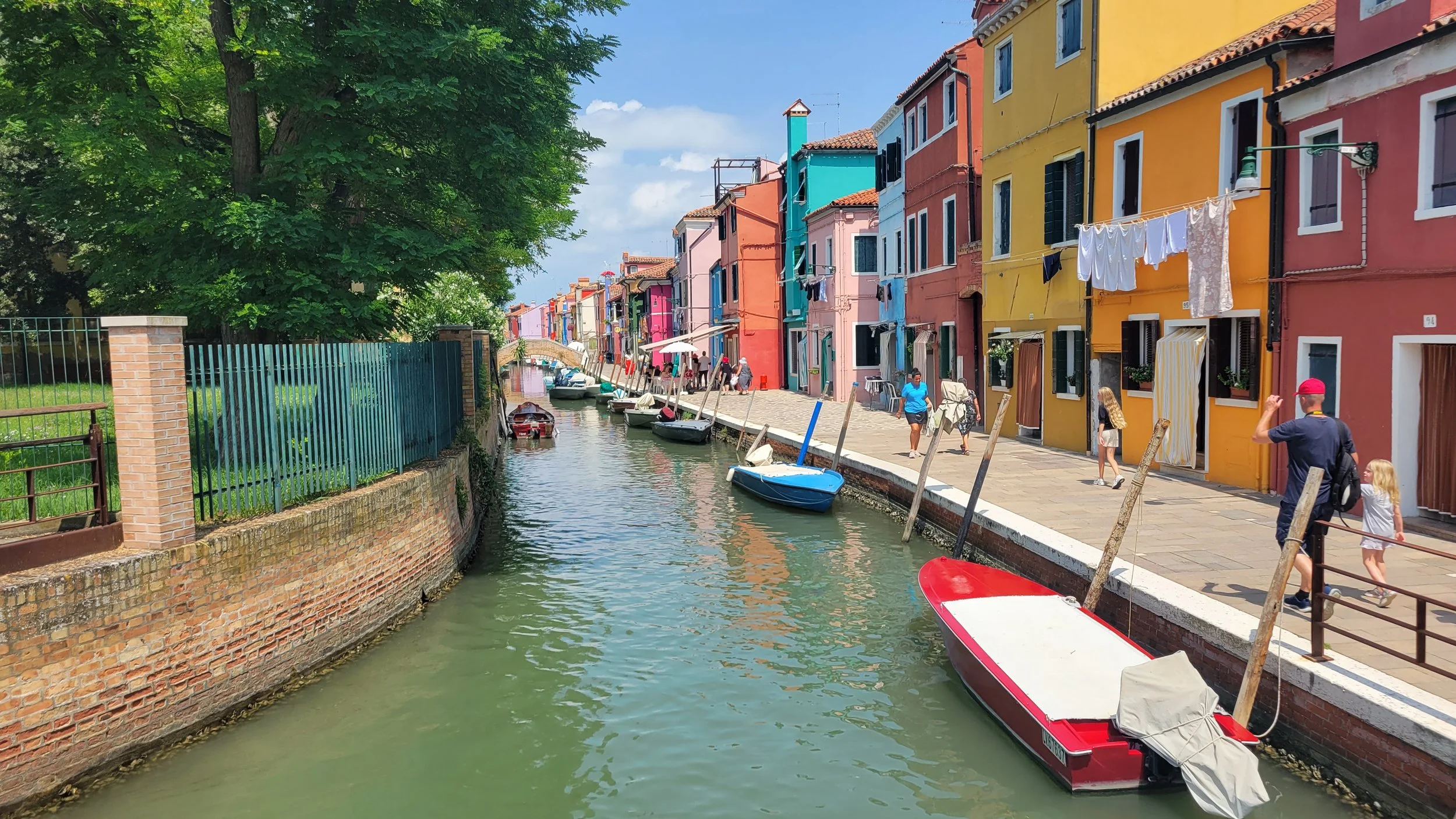 A canal in Venice, Italy where boats are in water and people are walking on sidewalk
