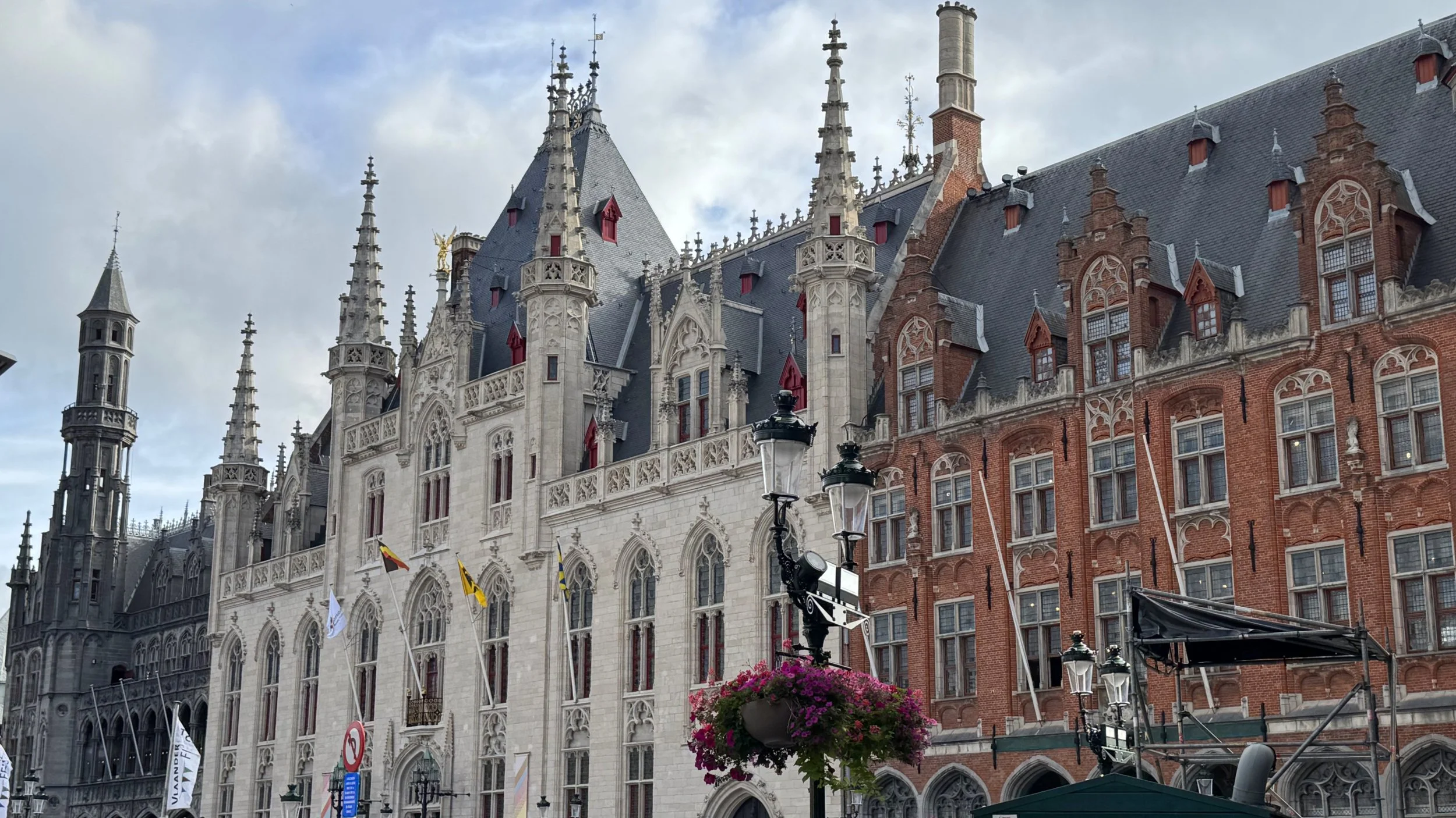A historic European building with Gothic architecture, featuring ornate spires, pointed arches, and detailed stonework. The building has a mix of white and red brick sections, numerous windows, and decorative elements.