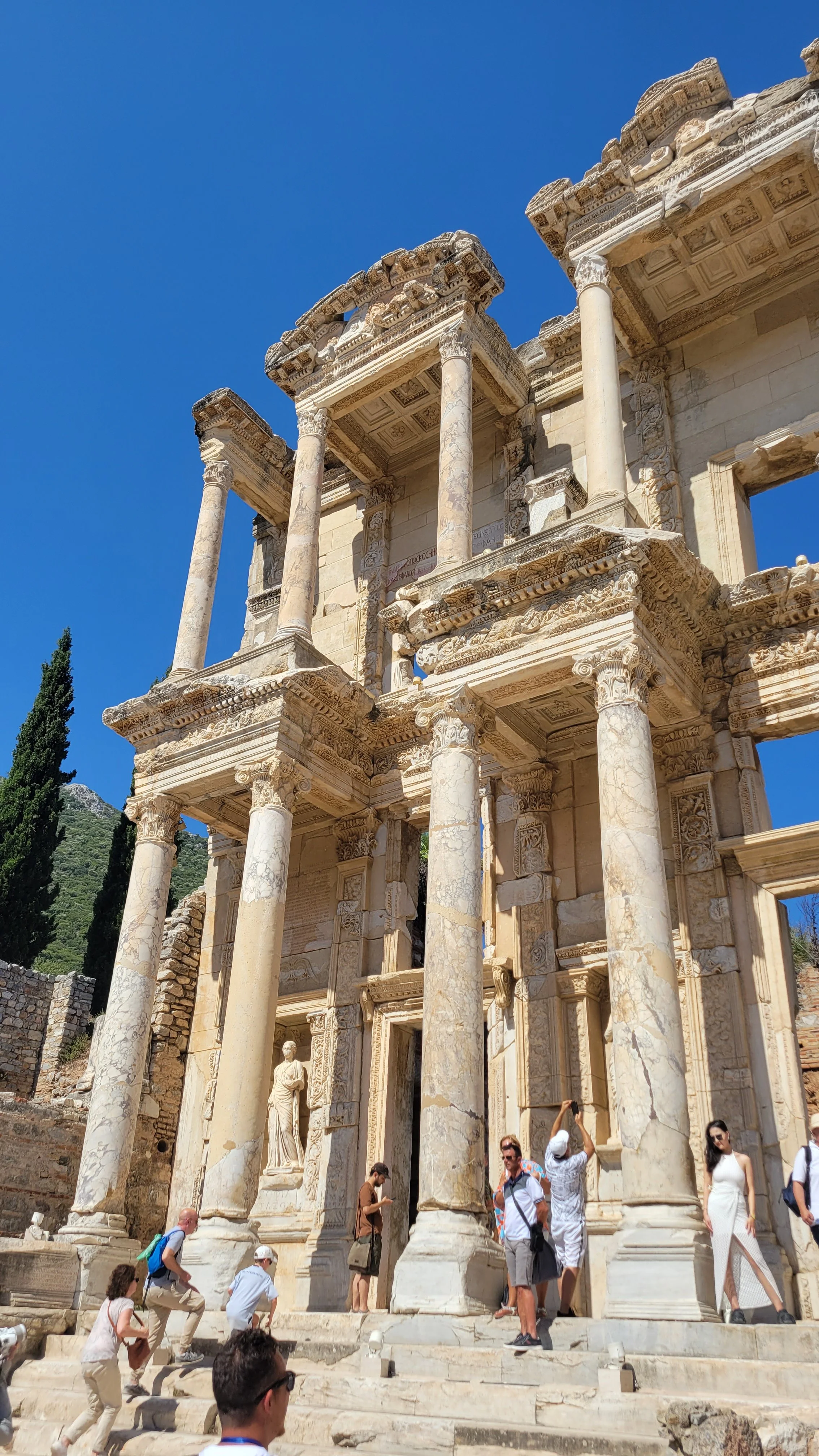 Ancient Roman ruins with tall marble columns and detailed carvings, with several tourists exploring and taking photos.