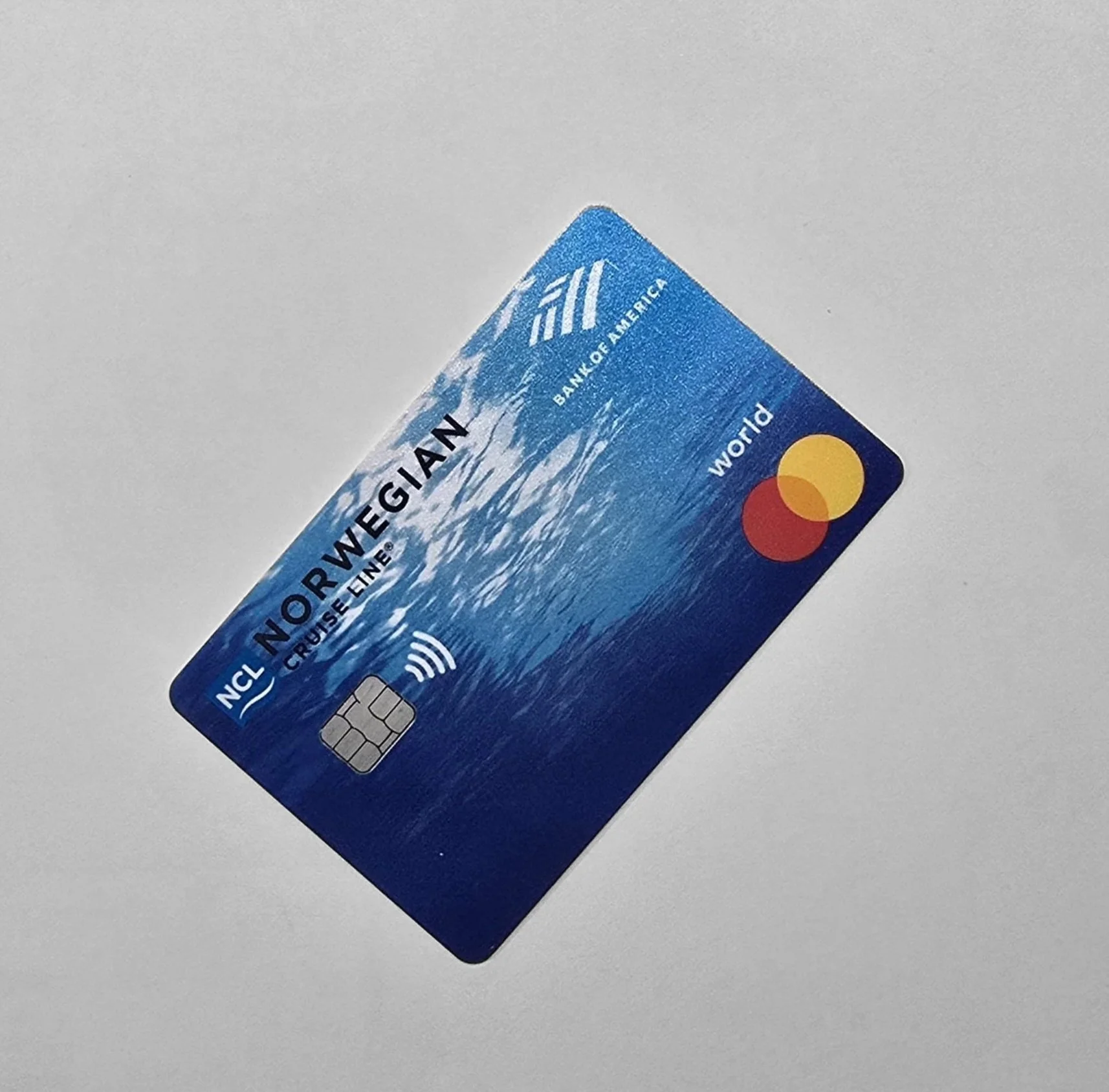 Blue credit card with mountain graphic, Mastercard logo, and contactless payment symbol on a white surface.