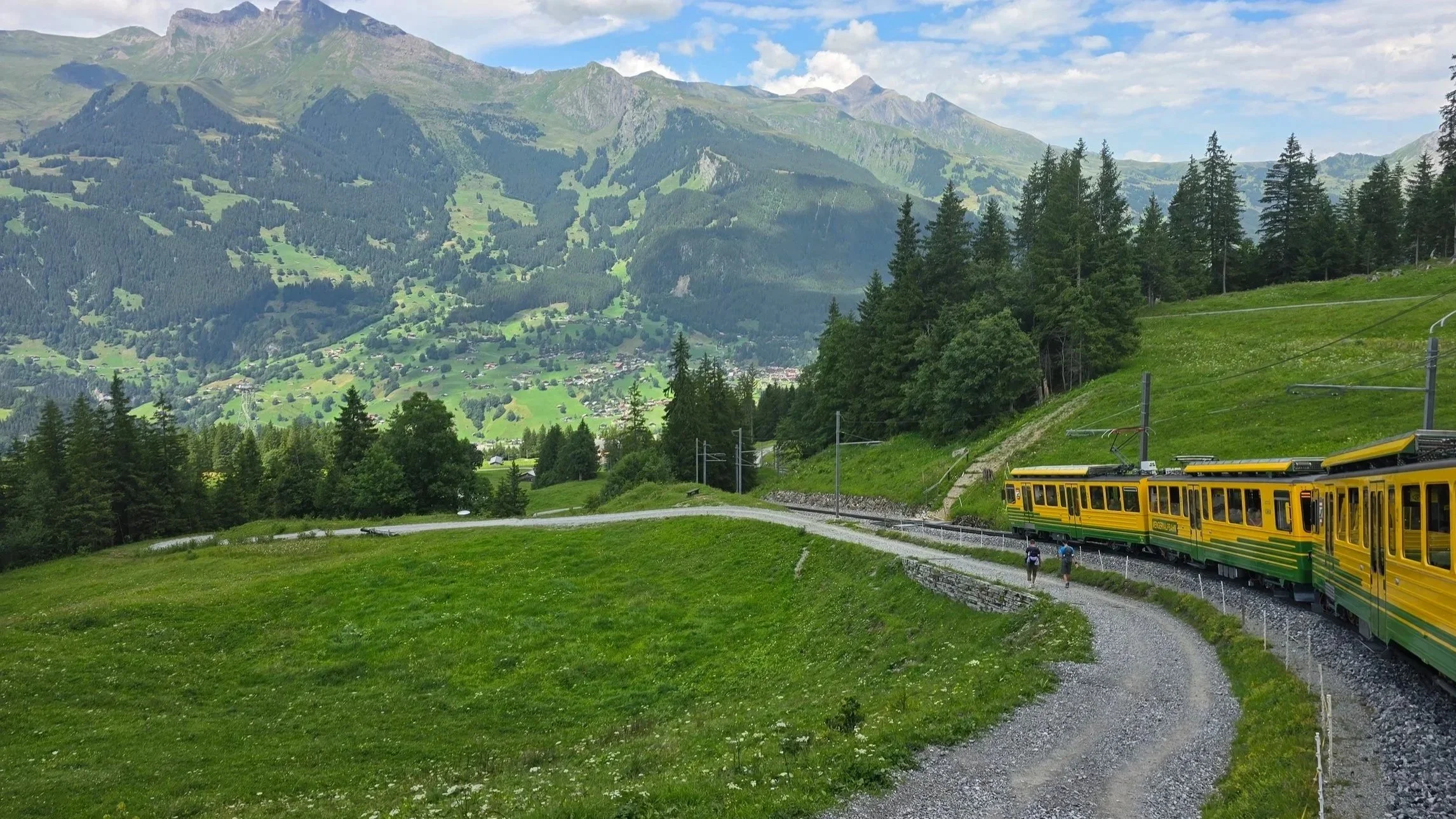 A green and yellow train traveling from Kleine Scheidegg to Grindelwald