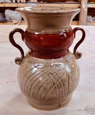 A ceramic vase with two handles and a decorative pattern, featuring a beige, brown, and reddish glaze.