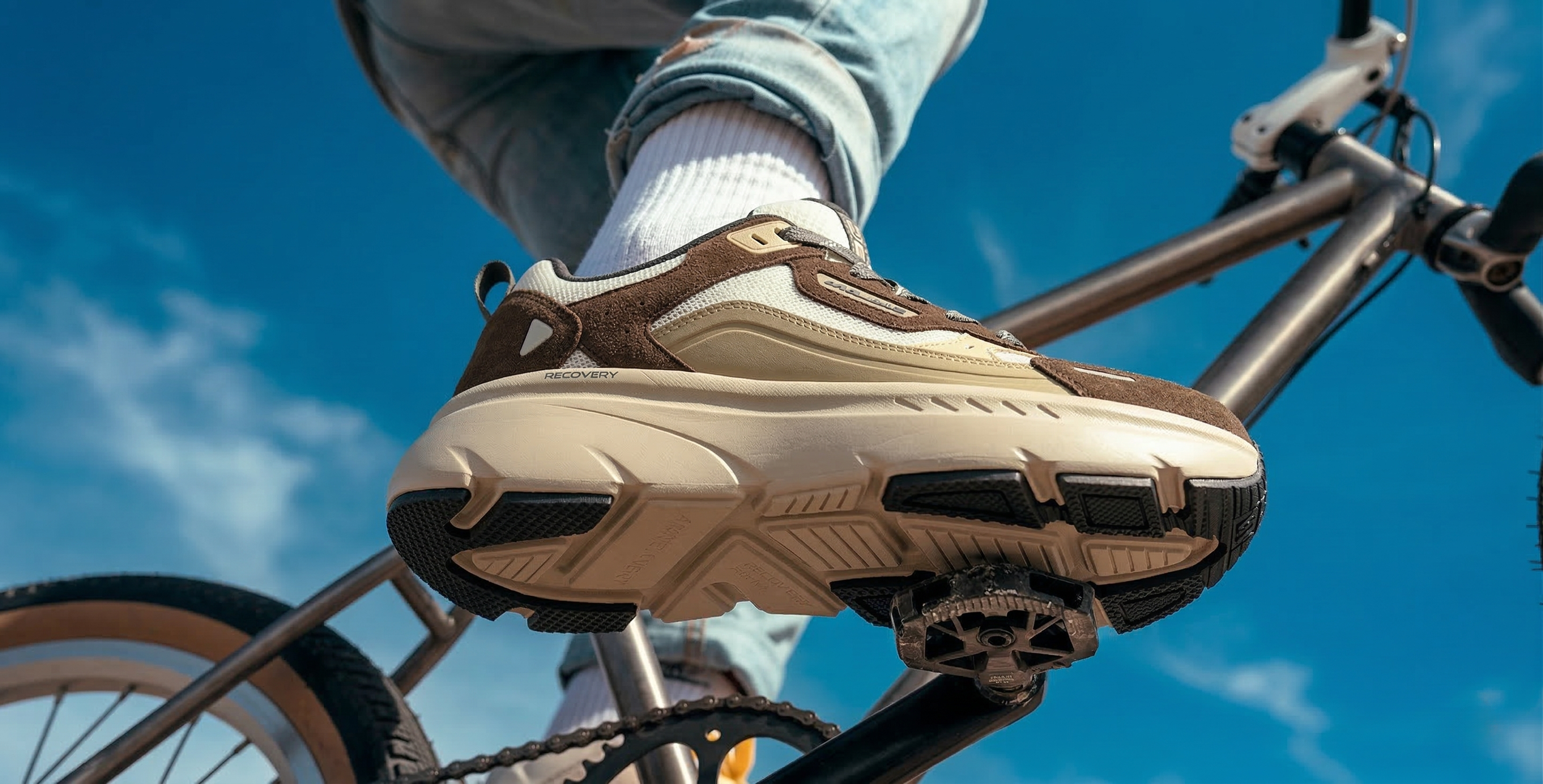 akiii-classic-recovery-sneaker-brown-beige-on-foot-bike-pedal-low-angle-blue-sky-01.png