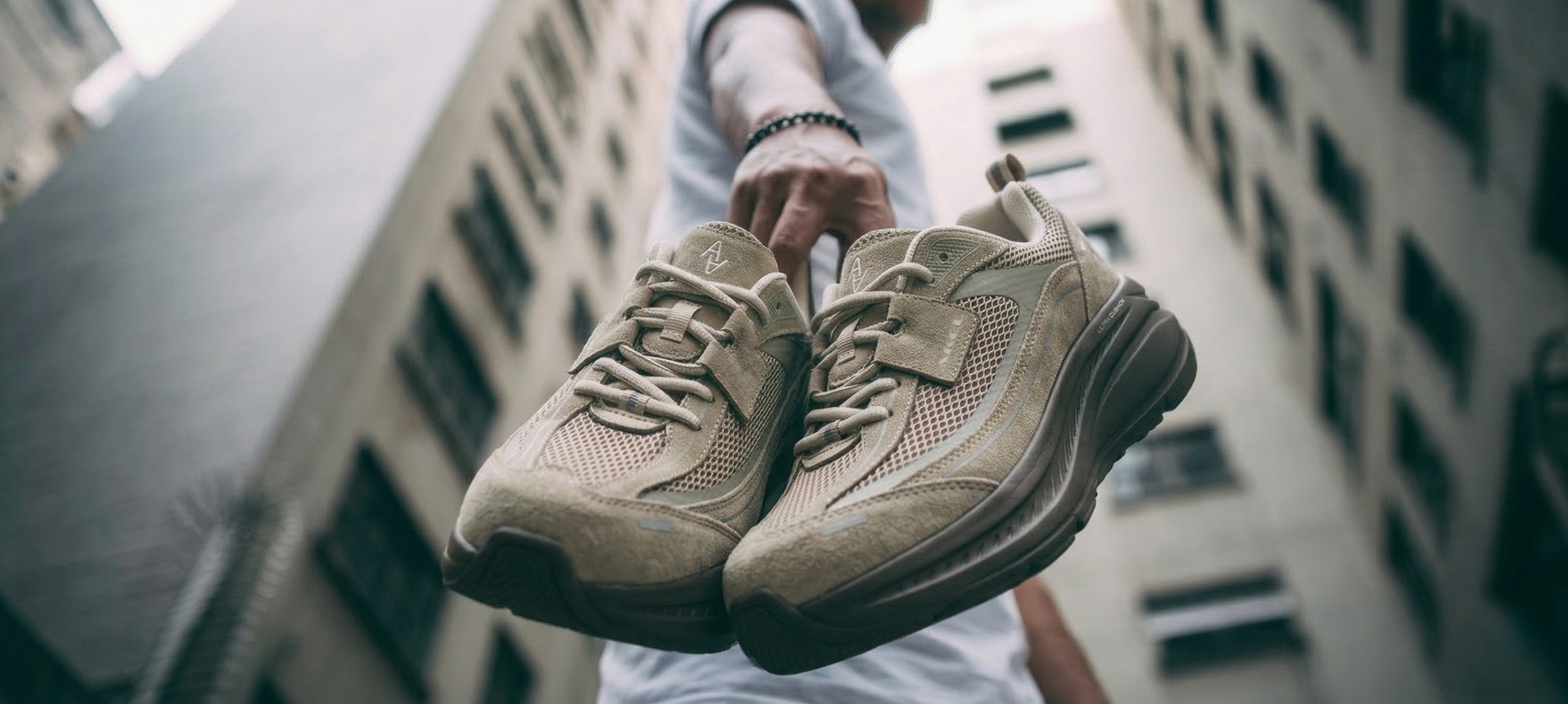 akiii-classic-recovery-sneaker-sand-beige-pair-hand-hold-low-angle-city-01.png