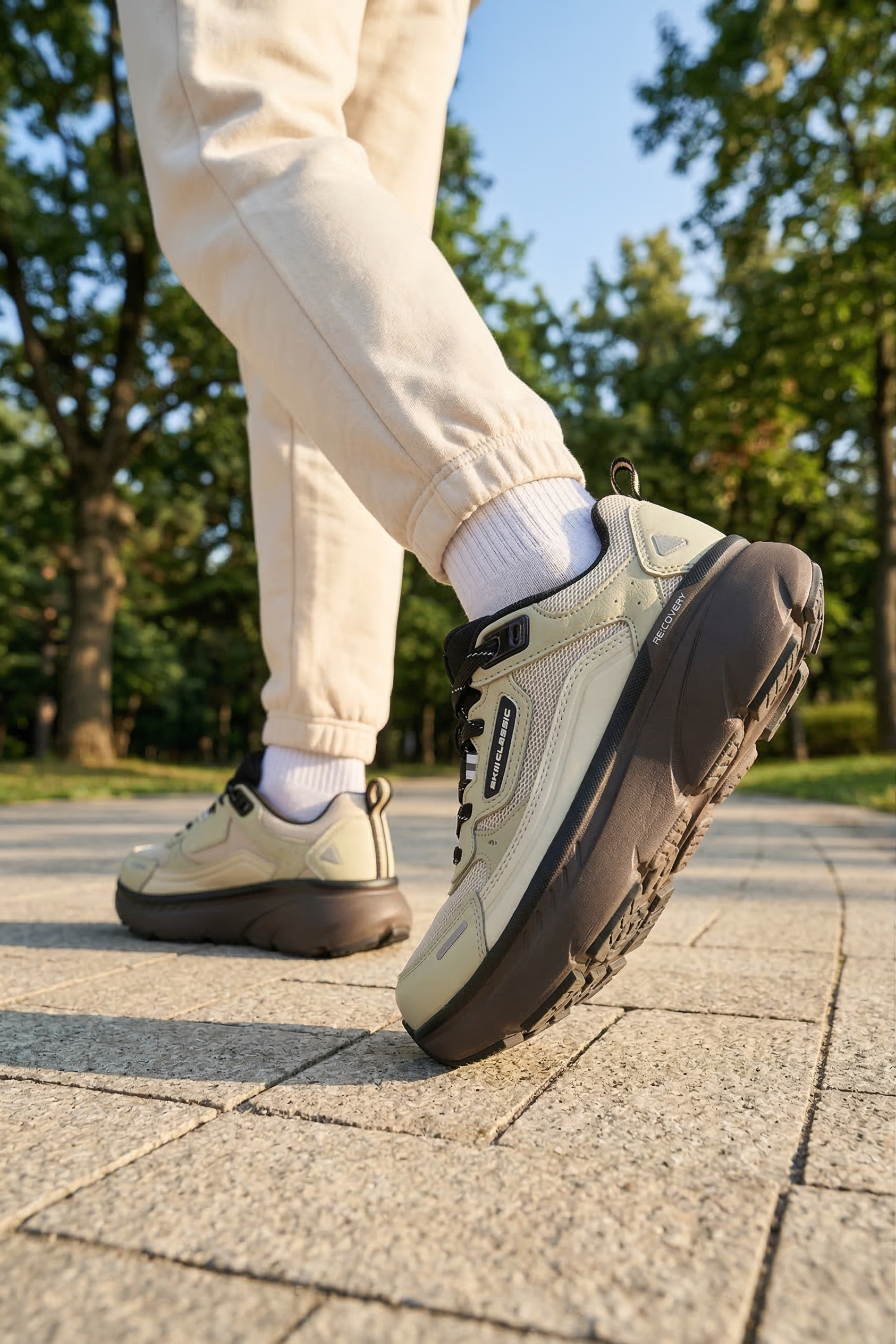 akiii-classic-recovery-sneaker-olive-green-on-foot-walking-heel-side-park-01.png