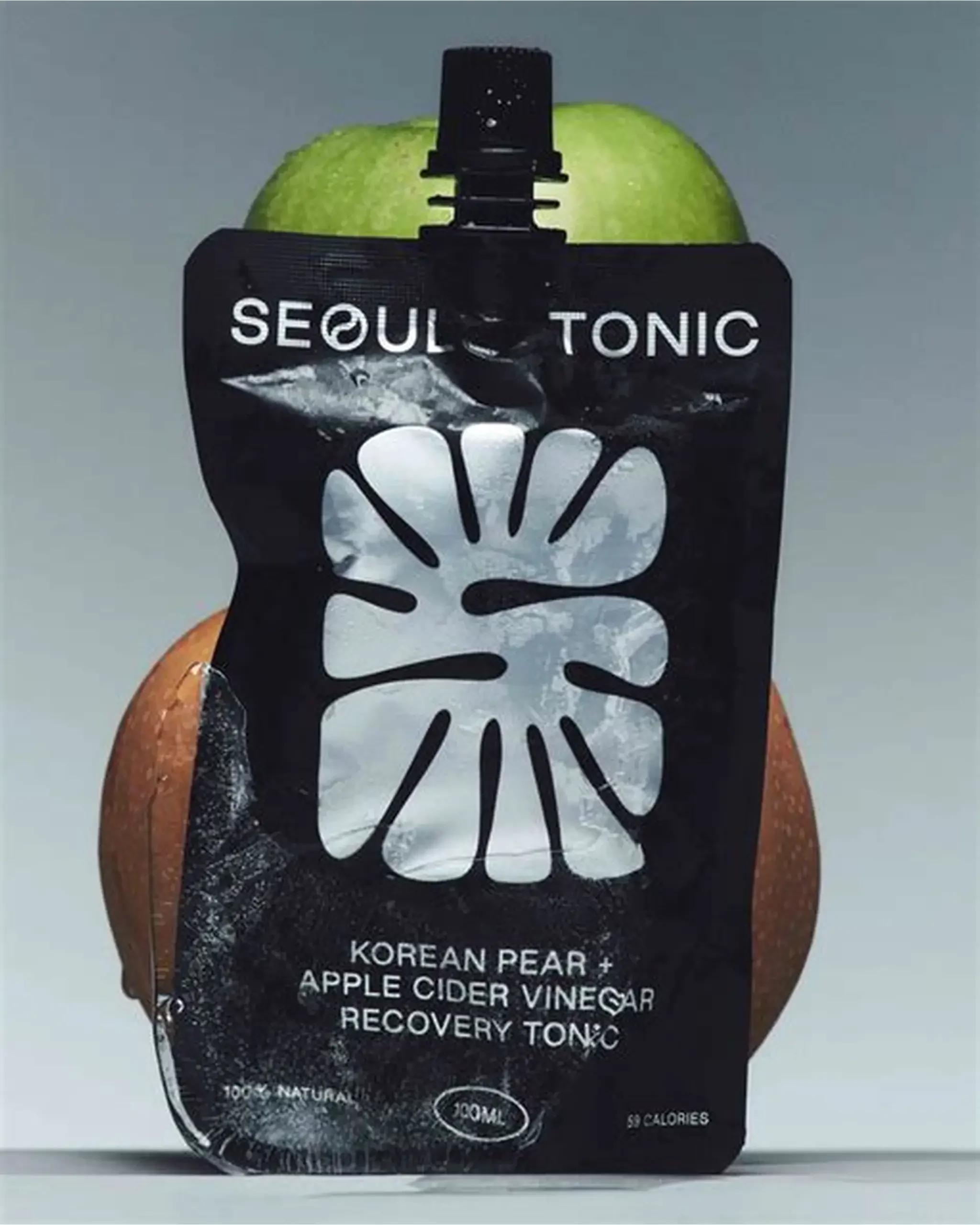 A black bottle of Korean pear and apple cider vinegar recovery tonic with a green apple in the background.