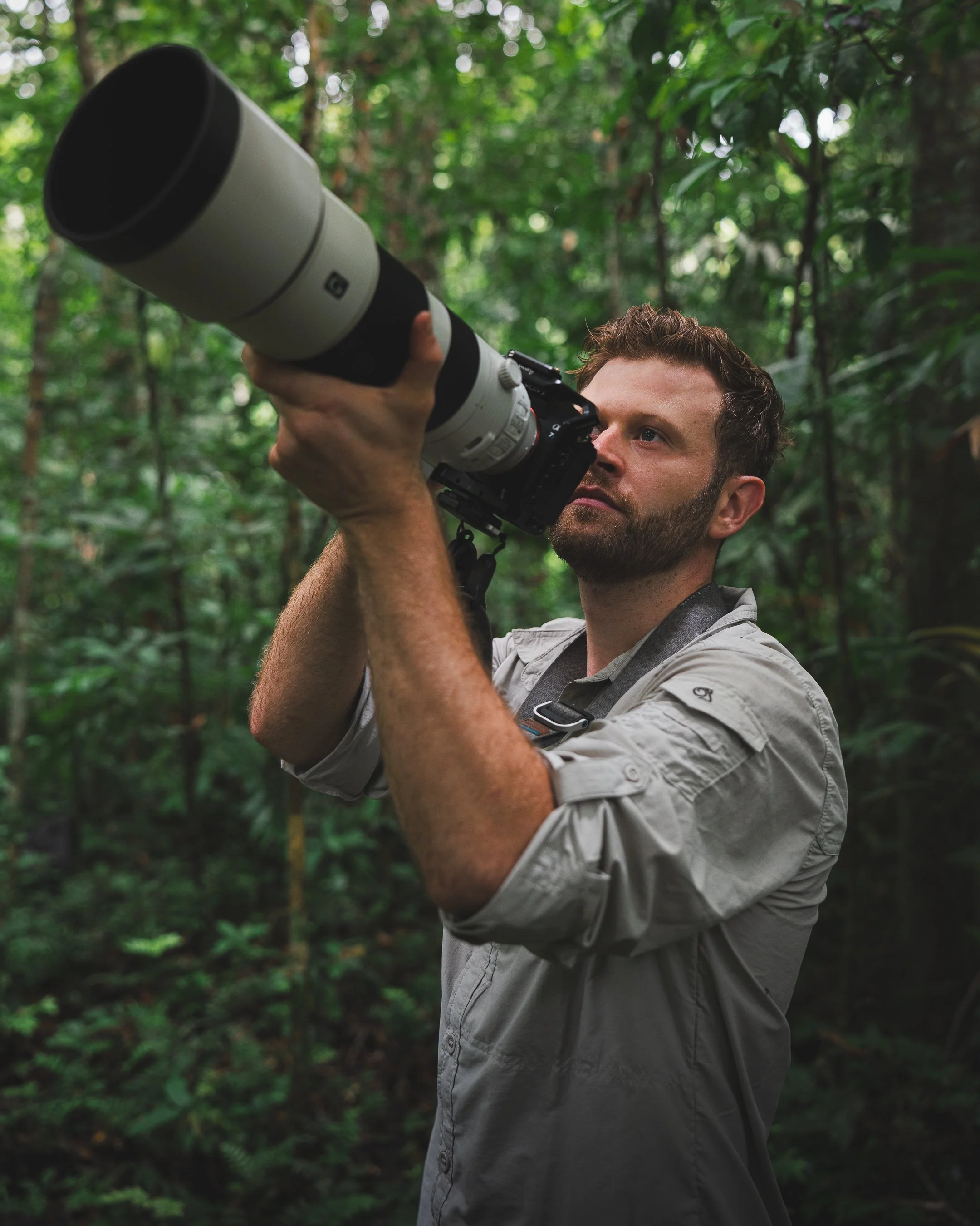 Luke Pembroke, a man with a beard and short curly hair taking a photograph with a large Sony 200-600mm telephoto lens in a dense green forest of the lowland Amazon rainforest in Peru on Wilderness International protected lands with Fauna Forever