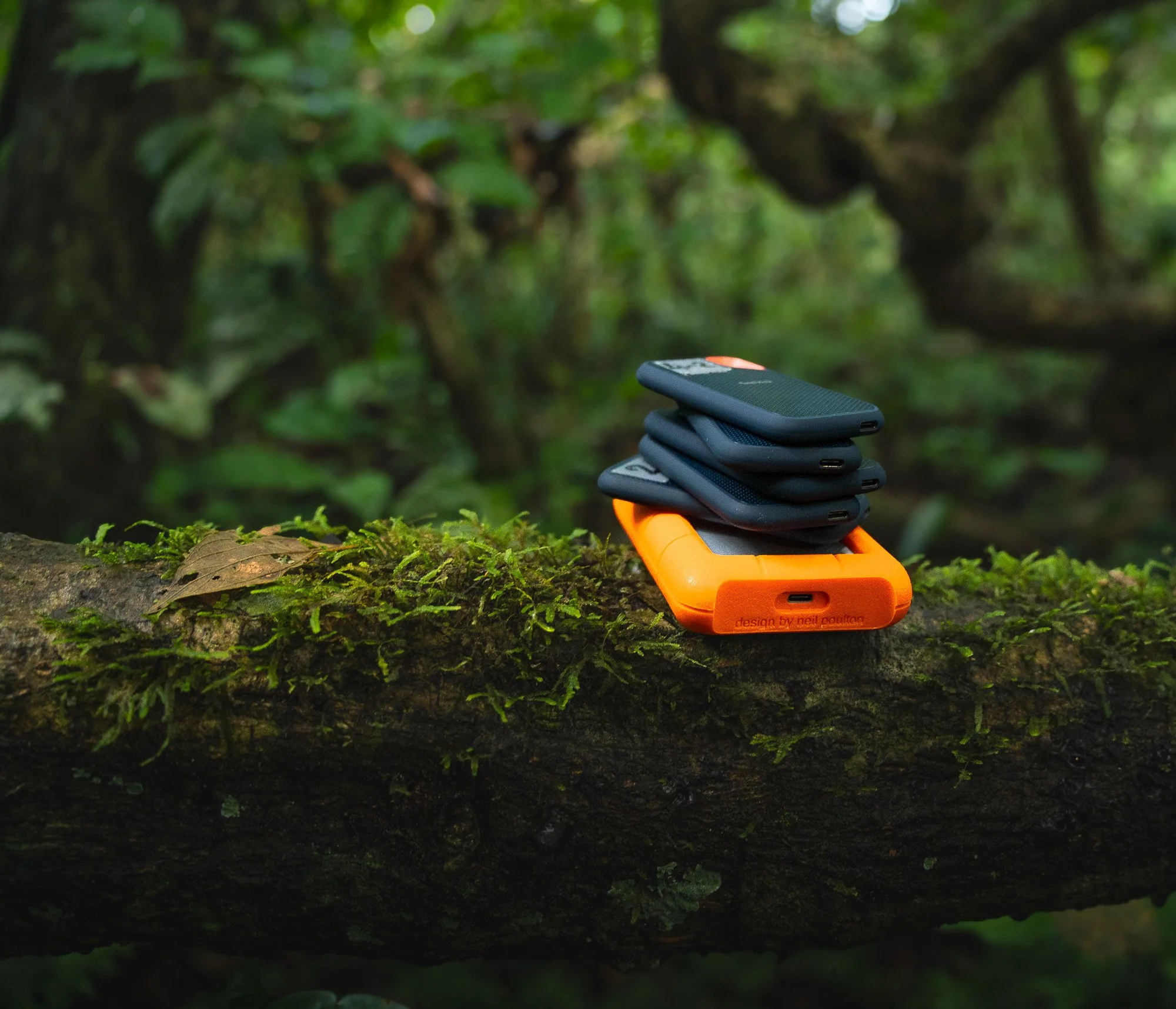 A stack of electronic devices, external SSD and HDD hard drives placed on a moss-covered log in a lush green forest of the amazon lowland rainforest, showing off the stock footage, that Foggy Lens Productions offers to buy