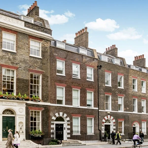Row of traditional brick townhouses with white window frames and green doors in an urban neighborhood.
