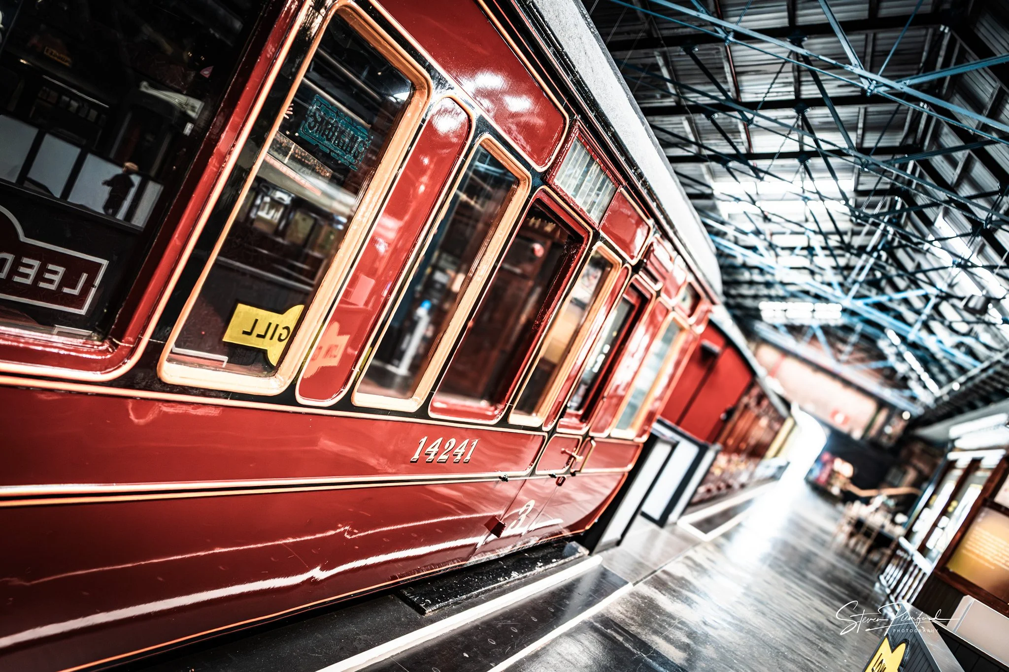 A vintage red train carrage with the number 14241, parked inside a station with a high ceiling and exposed blue steel beams.