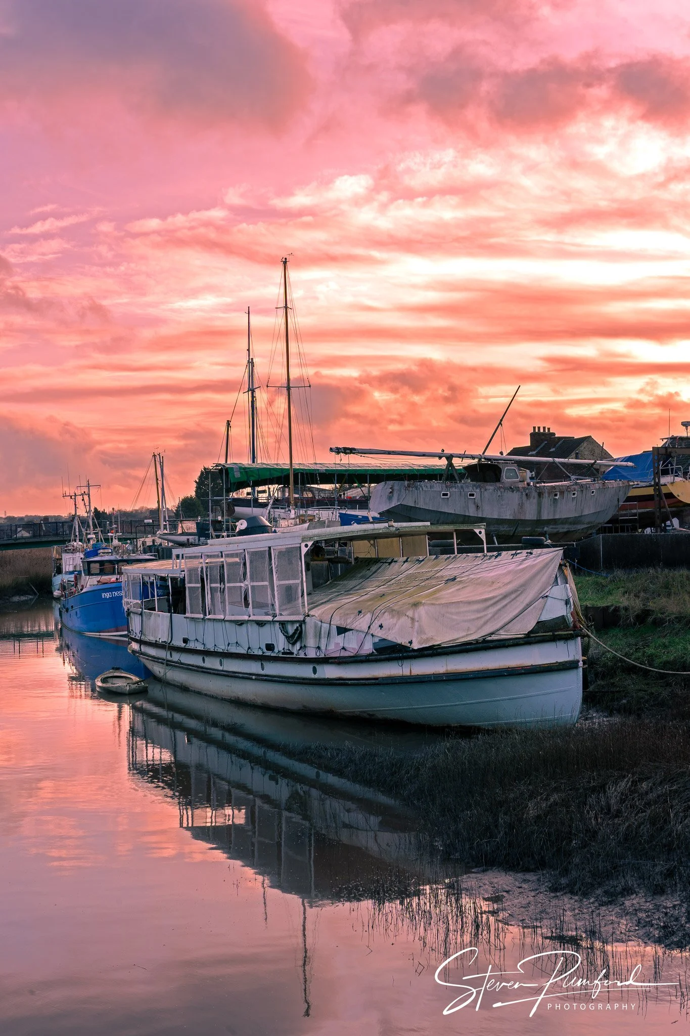 Sailboats docked in a calm body of water during a vivid pink and purple sunset with clouds in the sky.