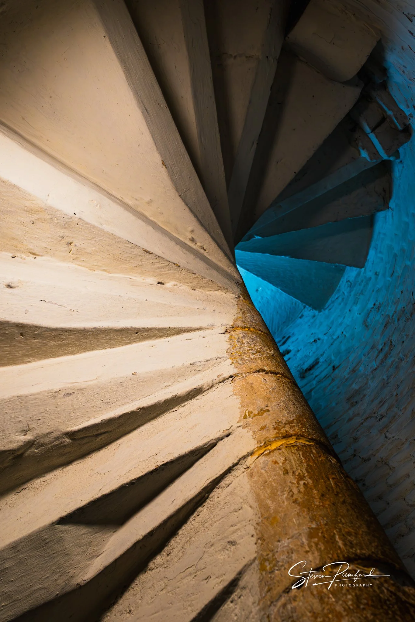 A staircase made of stone or concrete, captured from an angle looking upwards. The steps are weathered with visible marks and dirt. The lighting highlights textures and shadows on the steps, with a blue hue visible on some sections of the wall or wal