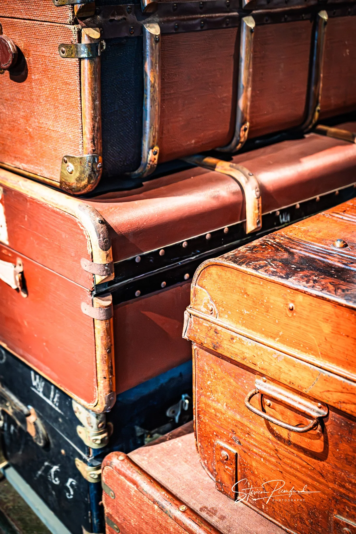 Close-up of vintage wooden suitcases with metal clasps and handles, stacked on top of each other, showing different shades of worn brown and red wood.