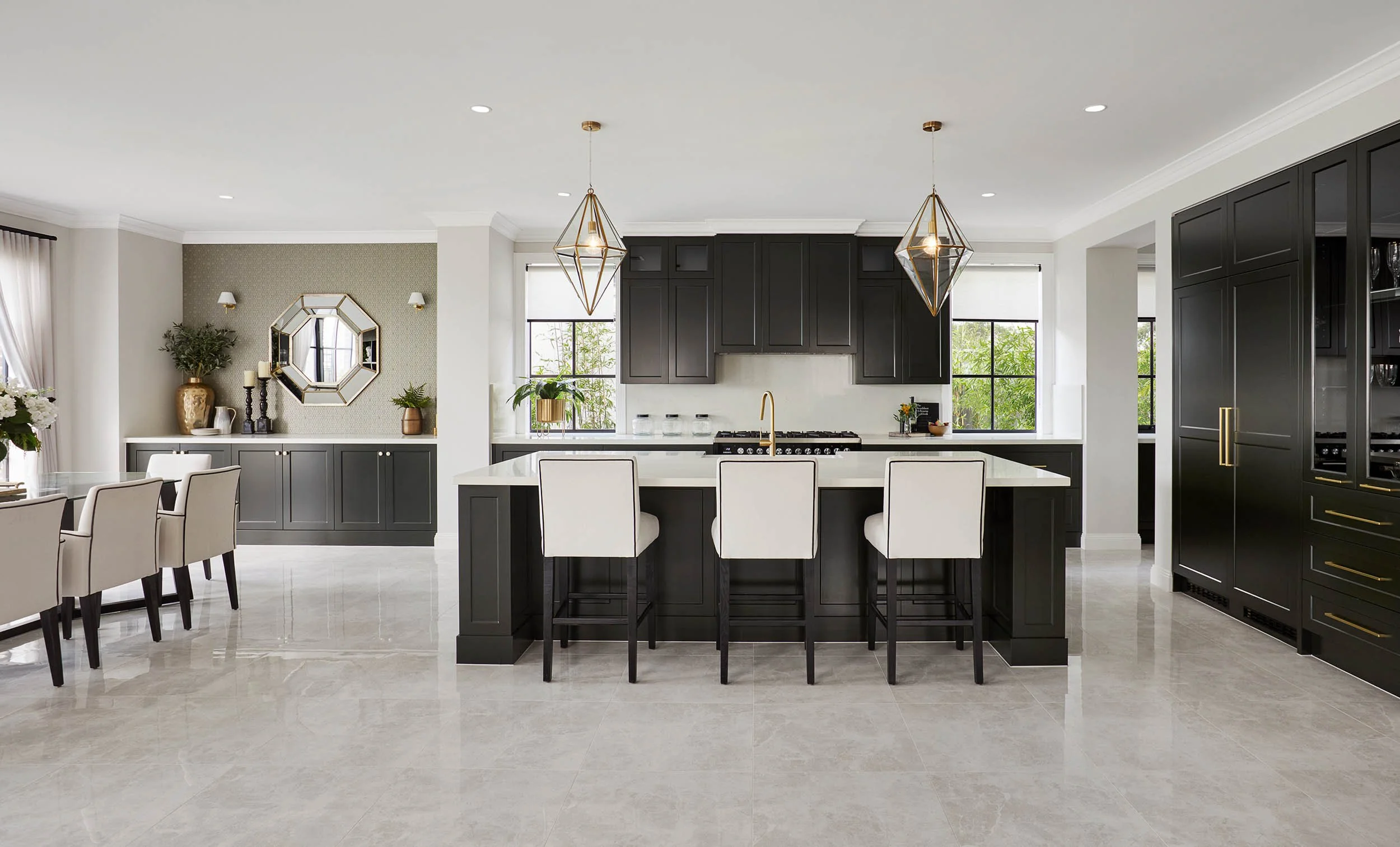 Modern kitchen with black cabinets, white countertops, a kitchen island, pendant lights, and a dining area with beige chairs and a window with curtains.