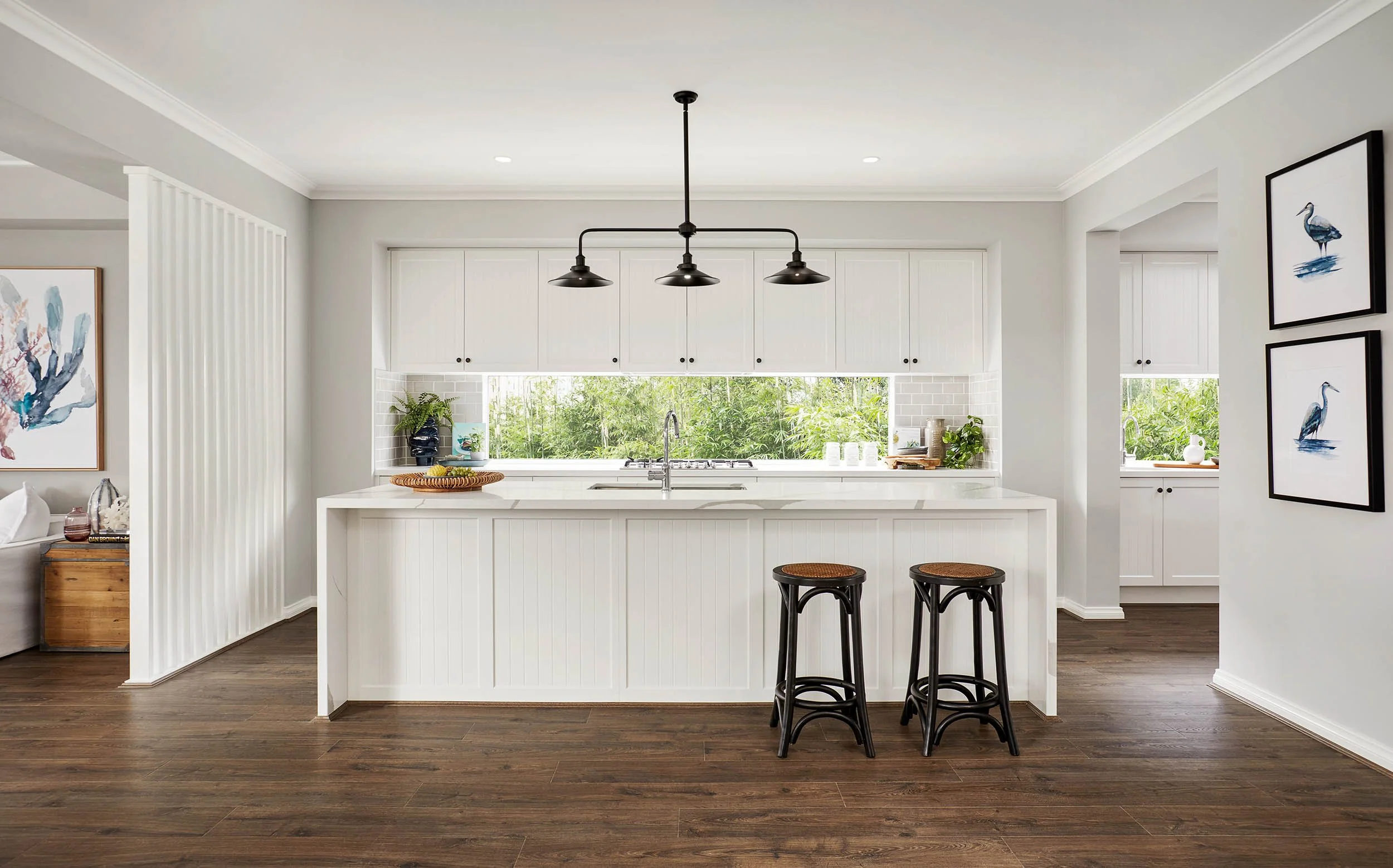 Modern kitchen with white cabinets, a large window overlooking greenery, and a kitchen island with four black bar stools.
