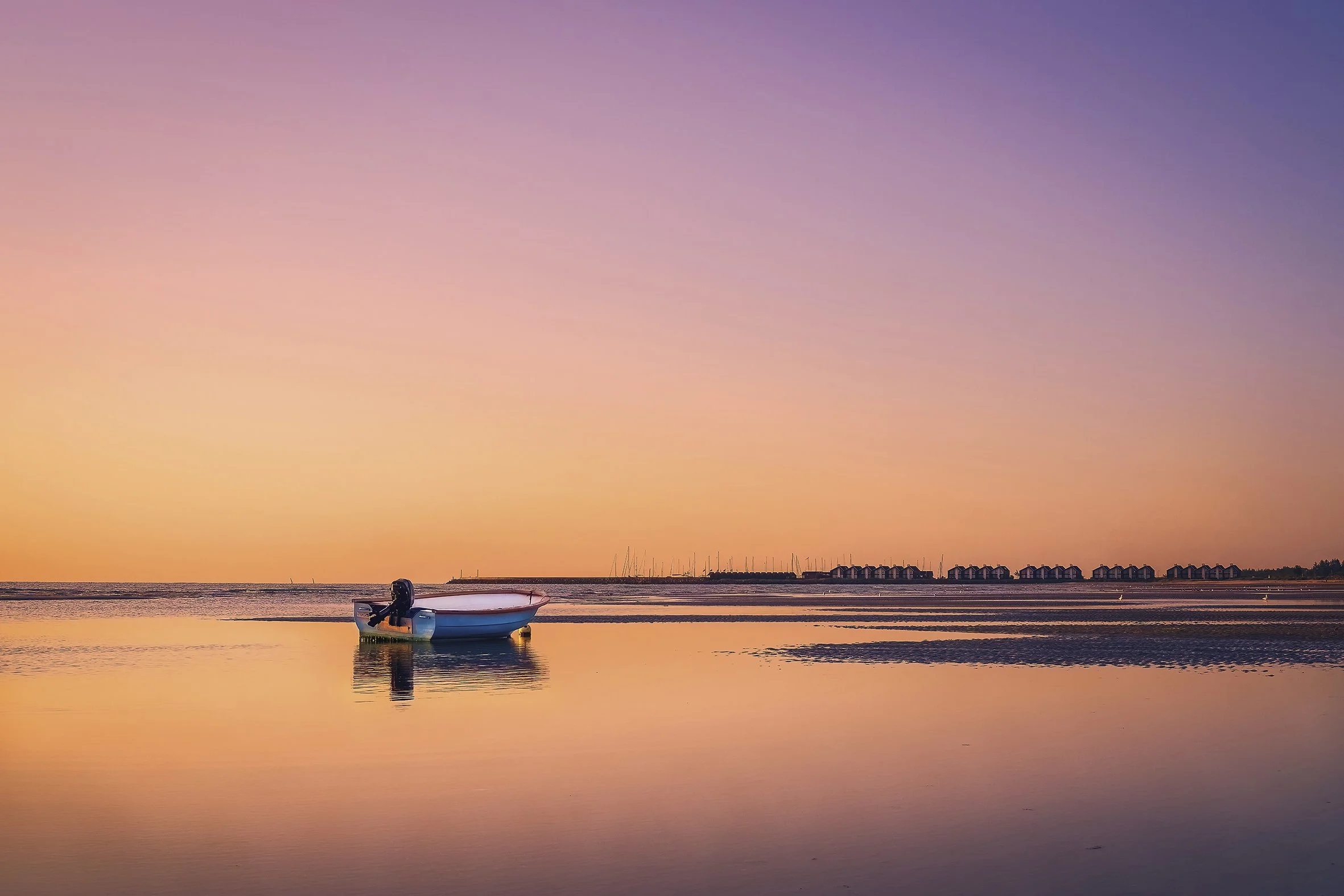 Small boat on calm shallow water at sunset, soft pastel sky and reflections, Denmark coastline
