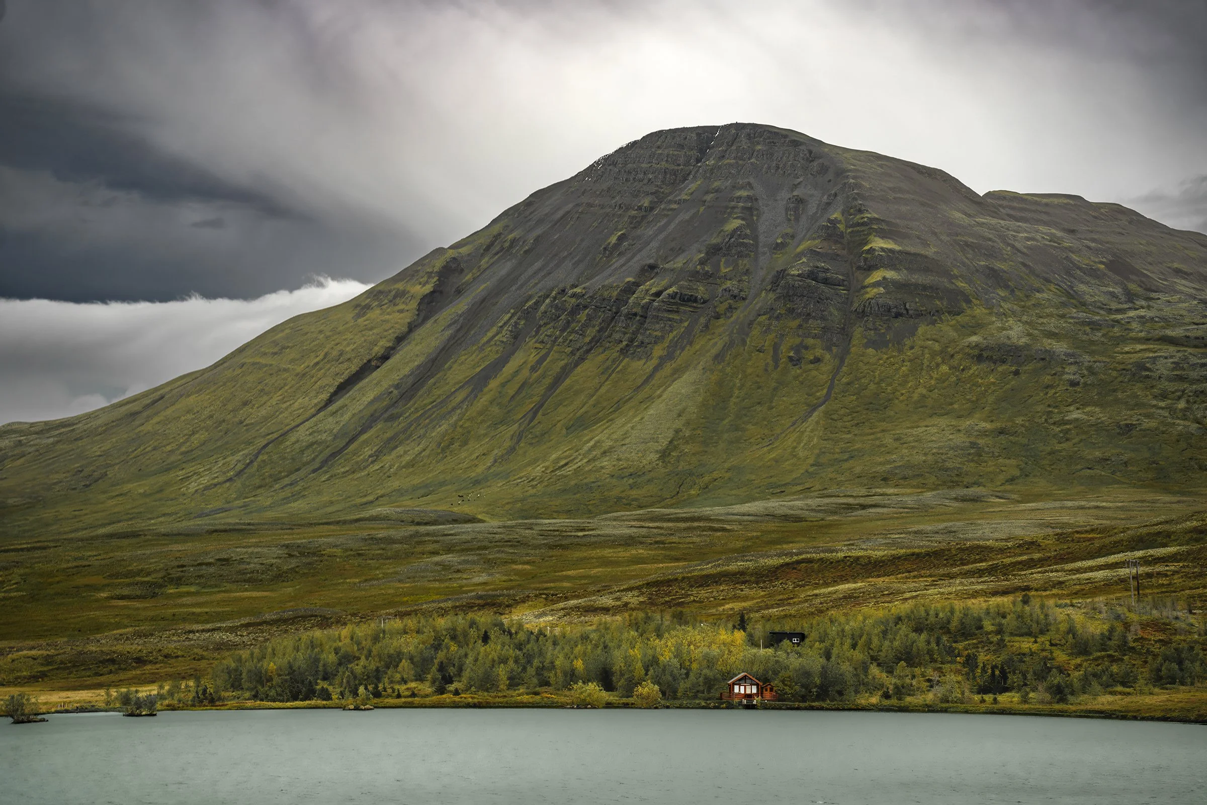 Remote cabin beneath dramatic mountain landscape in Iceland