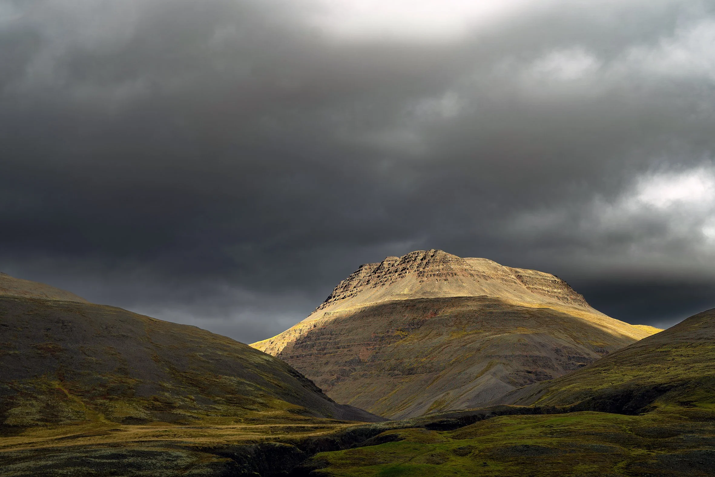 Dramatic photo of a mountain with light on the top and heavy clouds behind, from Iceland