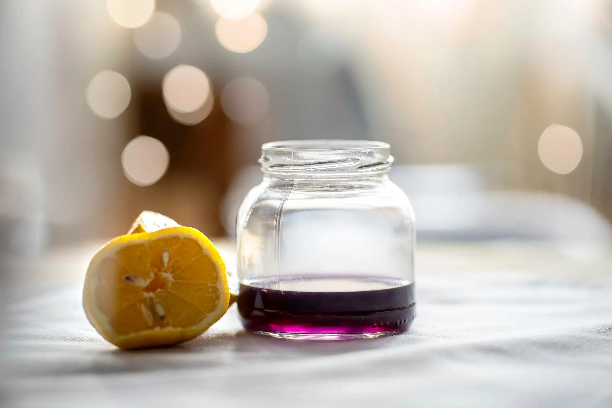 Minimal still life with glass jar, lemon and purple liquid in soft natural light
