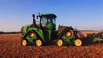 Green tractor working on a farmland field under clear blue sky