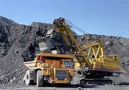 Large mining dump truck in a quarry with a yellow excavator loading material into it.