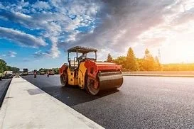 A yellow road roller compactor working on a highway during sunset.